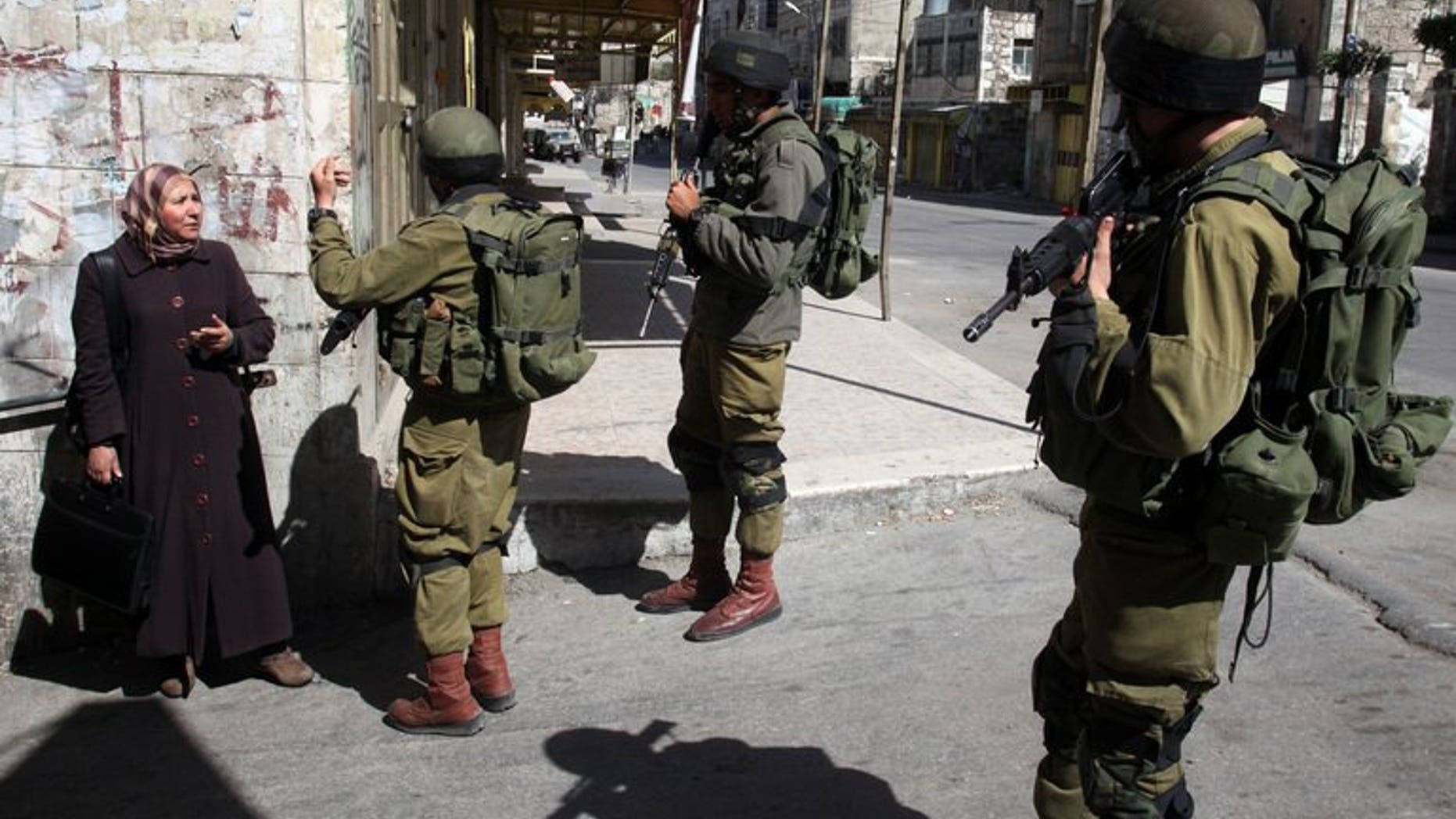 Israeli soldiers stop a Palestinian woman in the Palestinian side of the city of Hebron, on March 27, 2013.