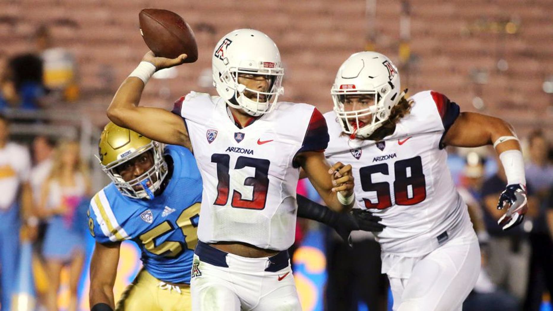 Arizona quarterback Brandon Dawkins (13) passes under pressure from UCLA defensive lineman Deon Hollins (58), left, with protection from Arizona offensive lineman Layth Friekh (58), right, in the first half of an NCAA college football game Saturday, Oct. 1, 2016, in Pasadena, Calif. UCLA won, 45-24. (AP Photo/Reed Saxon)