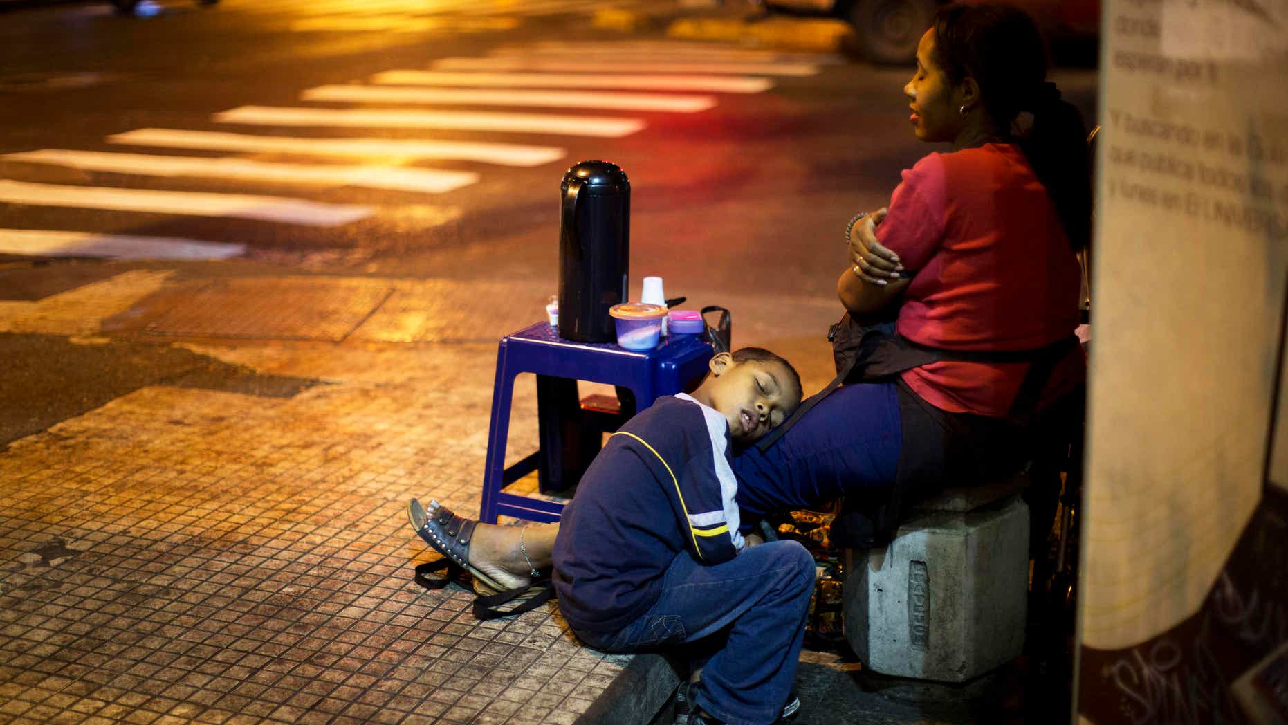 A child sleeps on the legs of his mother, who sells coffee in downtown Caracas, on March 4, 2014.