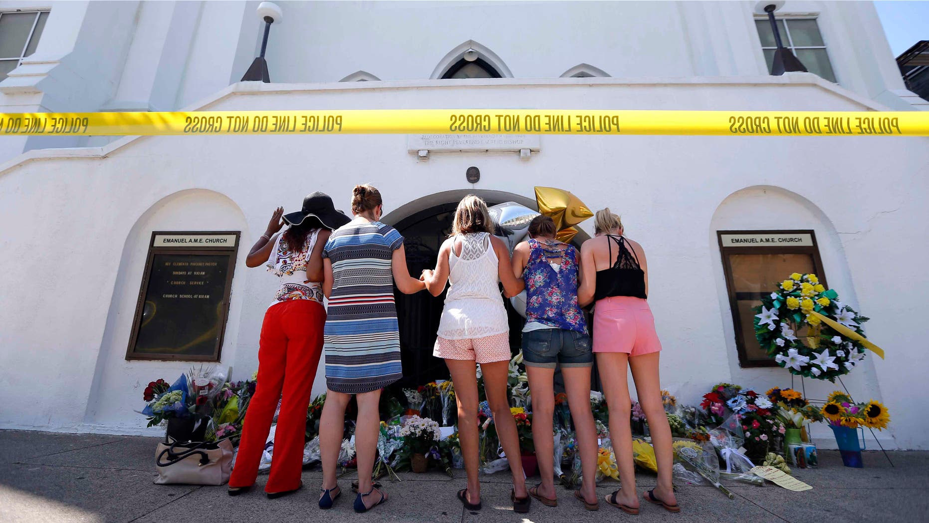 FILE- In this June 18, 2015, file photo, a group of women pray together at a makeshift memorial on the sidewalk in front of the Emanuel AME Church in Charleston, S.C. A single gunman shot and killed several people, including the pastor, at a prayer meeting inside the historic black church. In a poll conducted by the Associated Press and the Times Square Alliance found the most important news events to Americans in the past year were the shootings in Charleston, San Bernardino, Calif., Oregon and Tennessee. (AP Photo/Stephen B. Morton, File)