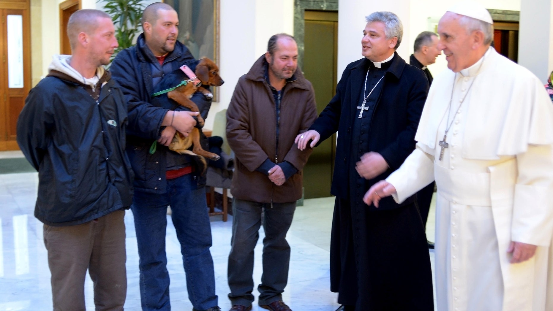 In this picture provided by the Vatican newspaper L'Osservatore Romano, Pope Francis, right, is flanked by Vatican Almoner Archbishop Konrad Krajewski as he welcomes four men at the Vatican, Tuesday, Dec. 17, 2013. Four homeless people, one of them bringing his dog, helped Pope Francis celebrate his 77th birthday at the Vatican Tuesday. They live on the street in the Rome neighborhood just outside the Holy See's walls and were invited by the Vatican official in charge of alms-giving to attend the morning Mass which Francis celebrates daily at the hotel where he lives on Vatican City grounds, the Vatican said. One of the men held his dog as he was presented to Francis after the guests chatted following Mass. The Vatican also said Francis invited his household help to join him in a "family-like" atmosphere, and he spoke of them one by one during his homily. (AP Photo/L'Osservatore Romano)