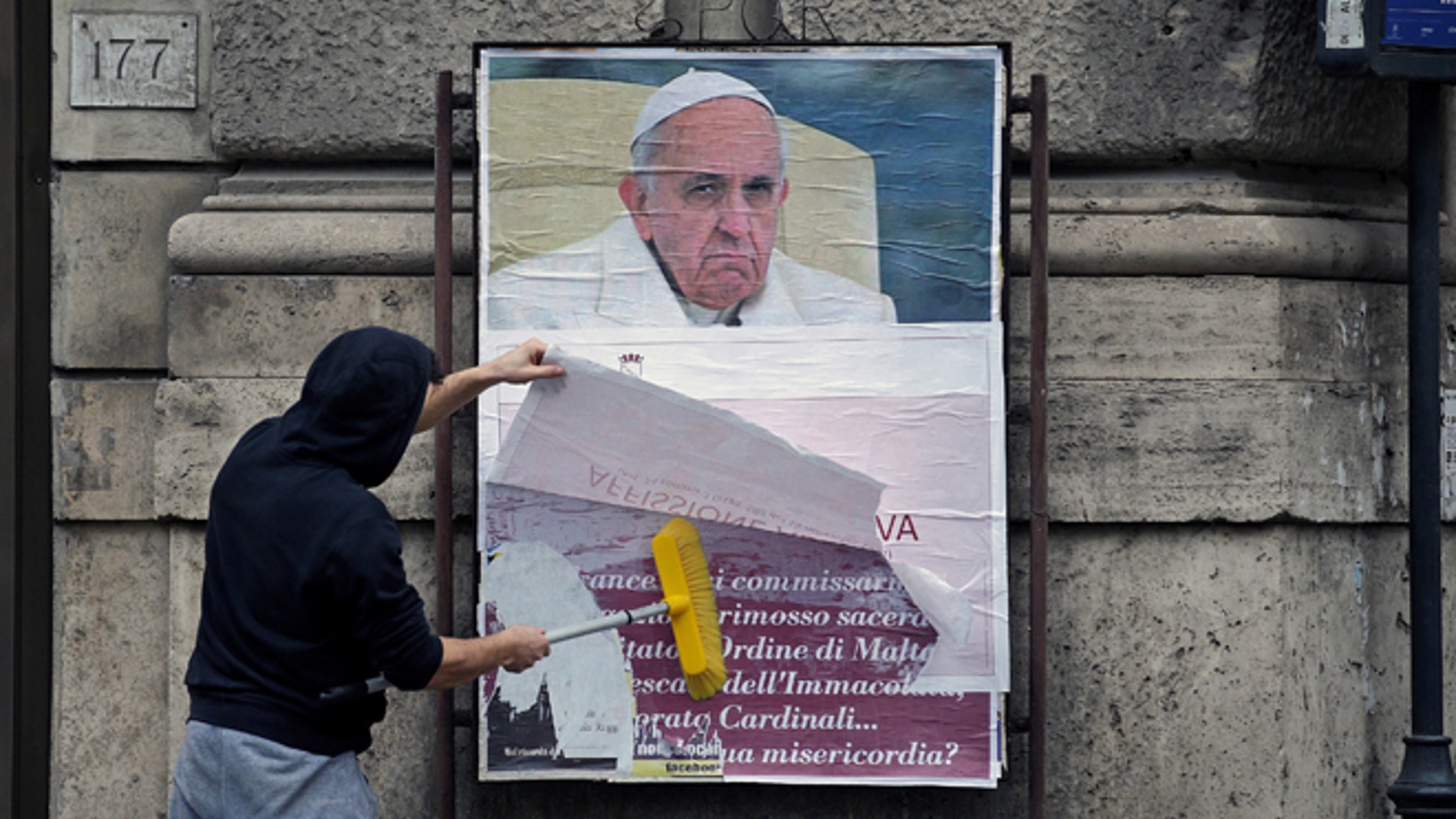 A worker covers a poster accusing the pope of attacking conservative Catholics in Rome, Italy, February 5, 2017