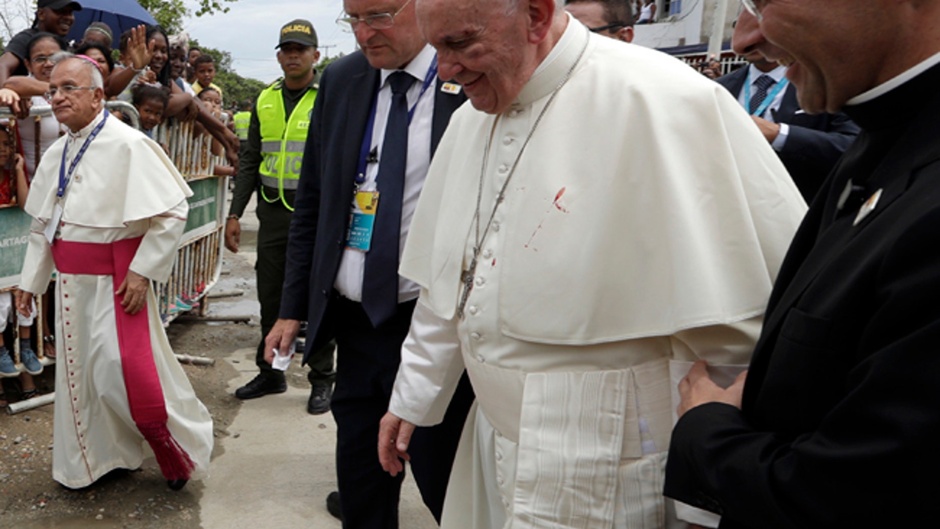 A small drop of blood stains Pope Francis' white cassock as he is helped by a priest, after knocking his head on the popemobile in Cartagena, Colombia, Sunday, Sept. 10, 2017.