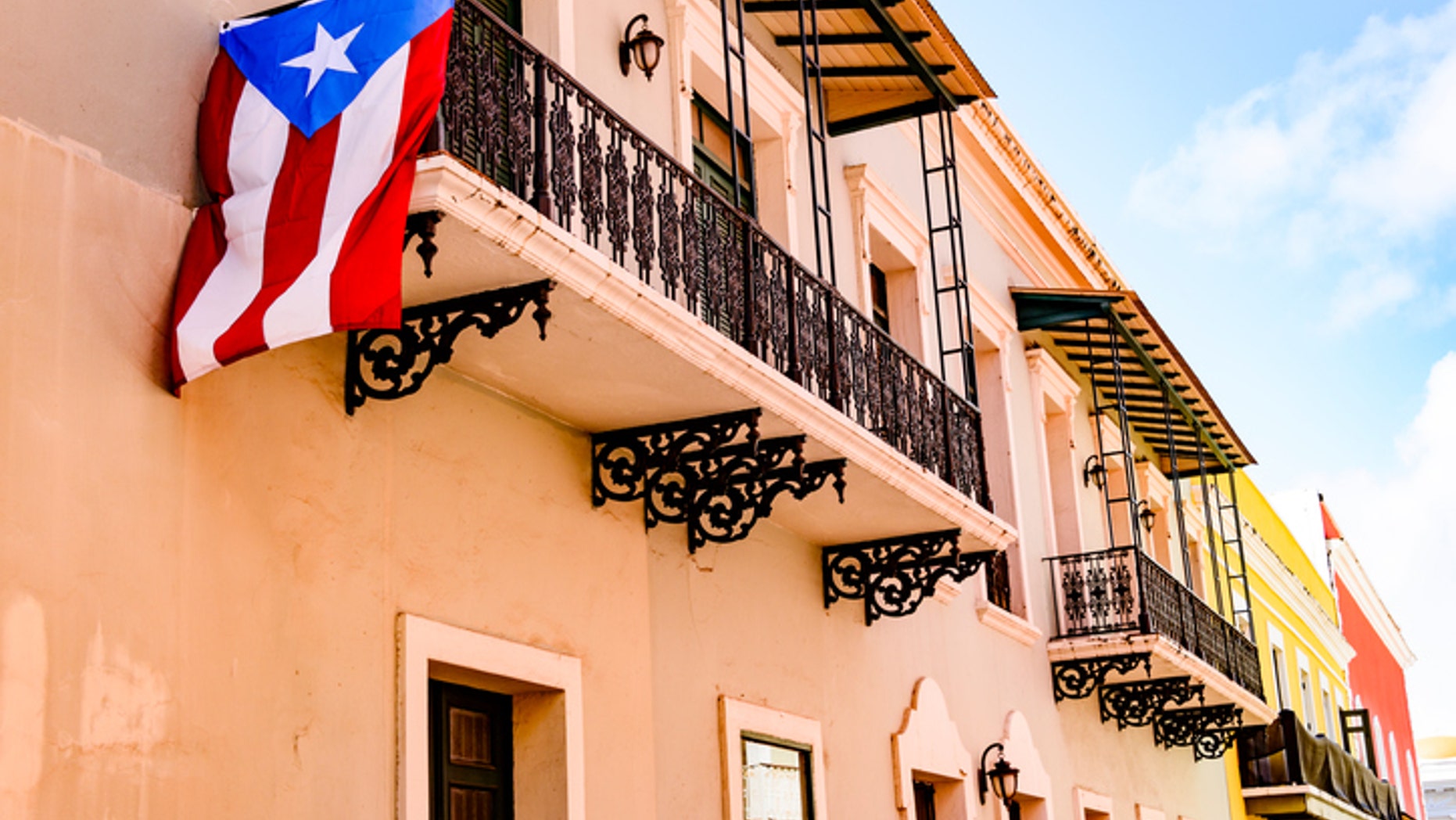 Colorful house facades along a street in Old San Juan, Puerto Rico with a Puerto Rican flag hanging down from one of the balconies