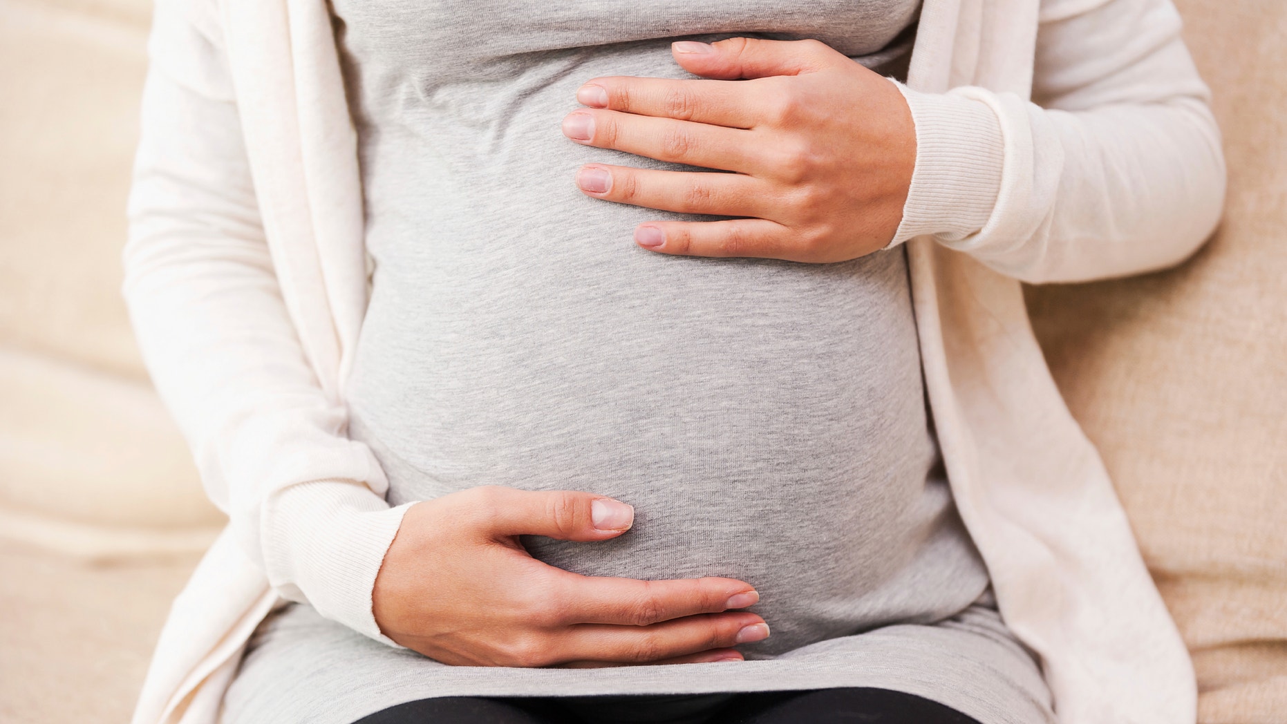 Waiting for a baby. Close-up of young pregnant woman touching her abdomen while sitting on the couch