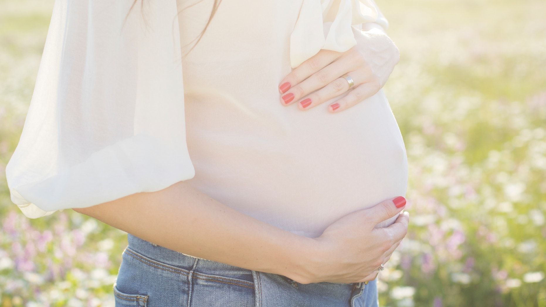 Happy pregnant woman is sitting in meadow of chamomile flowers, sunset time, new life concept