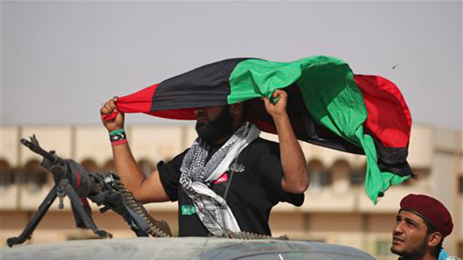 A former rebel fighter holds a pre-Gadhafi's flag at the northern gate of Bani Walid, Libya, Monday, Sept. 19, 2011.