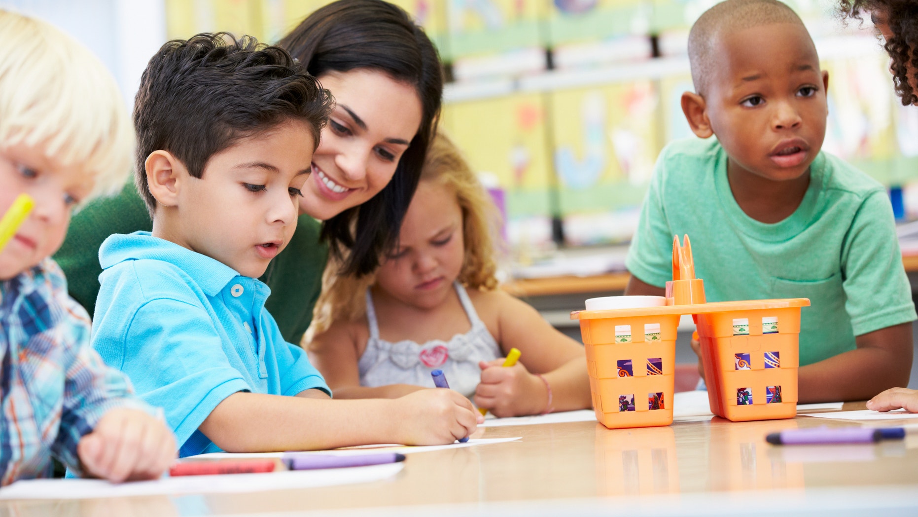 Group Of Elementary Age Children In Art Class With Teacher Using Crayons Drawing
