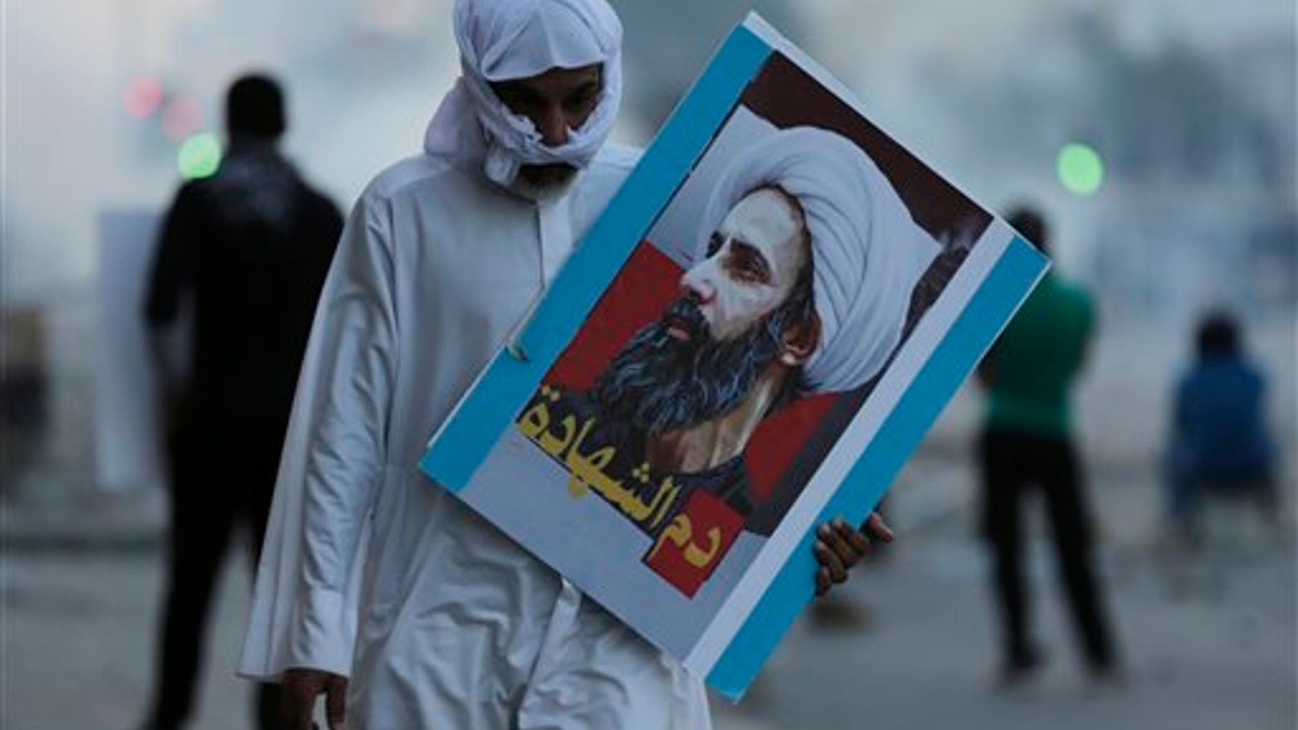 A Bahraini protester carries a picture of Saudi Shiite cleric Sheikh Nimr al-Nimr that reads, "blood of the martyr," during clashes with riot police in Sitra, Bahrain, Friday, Jan. 8, 2016. (AP Photo/Hasan Jamali)