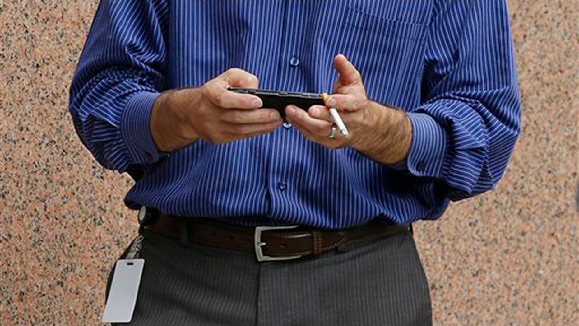 A man checks his cell phone while smoking outside an office building, Tuesday, July 21, 2015, in Providence, R.I. Providence is considering an ordinance that would prohibit smoking throughout downtown.