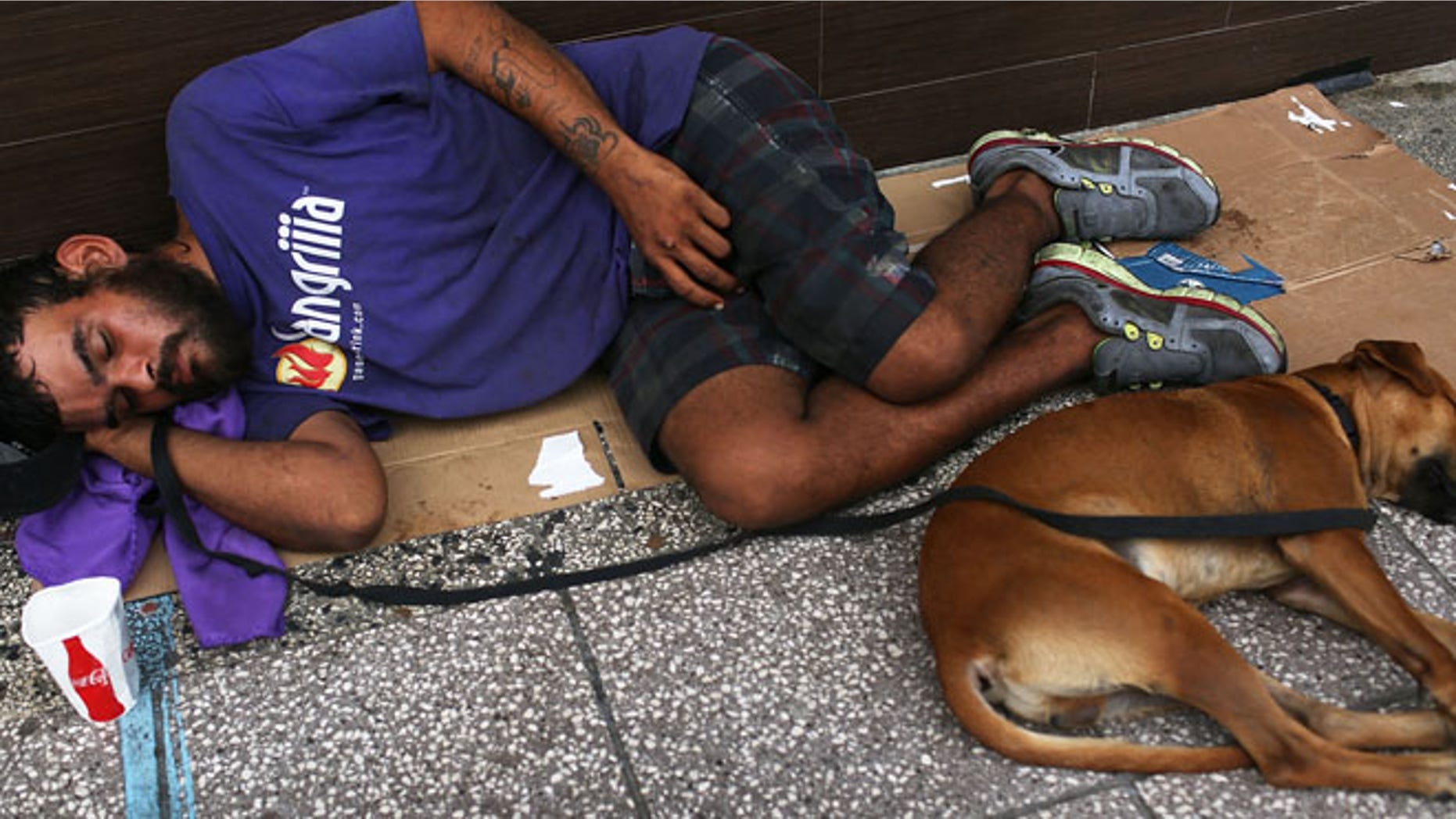 SAN JUAN, PUERTO RICO - JULY 01: A man sleeps on the sidewalk with a dog on July 1, 2015 in San Juan, Puerto Rico. The island's residents are dealing with increasing economic hardships and a financial crisis that has resulted in the government's $72 billion debt. Governor Alejandro Garcia Padilla said in a speech recently that the people will have to sacrifice and share in the responsibilities for pulling the island out of debt. (Photo by Joe Raedle/Getty Images)