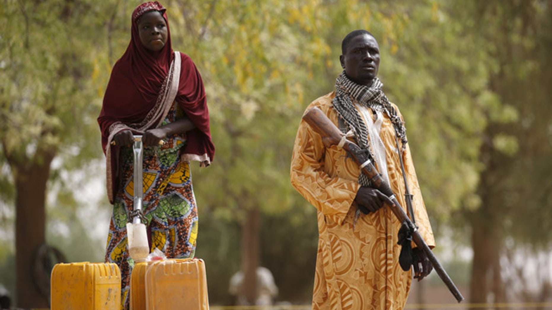 March: A member of a civilian vigilante group holds a hunting rifle while a woman pumps water into jerrycans in Kerawa, Cameroon. Kerawa is on the border with Nigeria and is subject to frequent Boko Haram attacks.