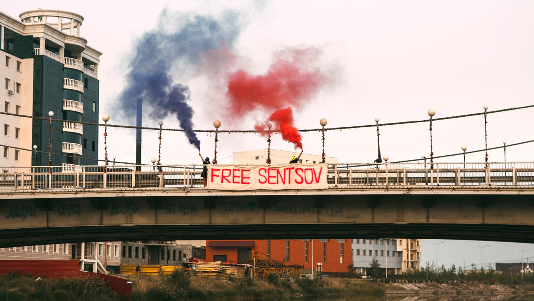 In this handout photo taken on Sunday, Aug. 6, 2017 and released on Monday, Aug. 7, 2017 by Zona.media, Maria Alyokhina and Olga Borisova, members of the Russian punk band Pussy Riot, hold flares and a banner on the bridge nearby outside the prison colony in Yakutsk, Russia, Monday, Aug. 7, 2017.