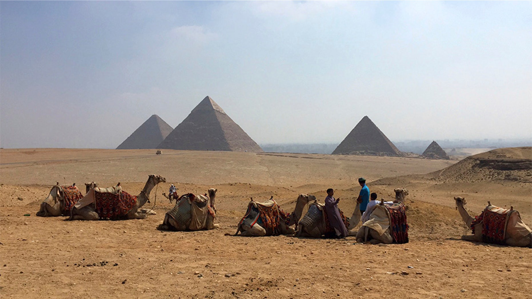 Camels rest between rides with their owners against the backdrop of the pyramids in Giza, Egypt, in 2015.