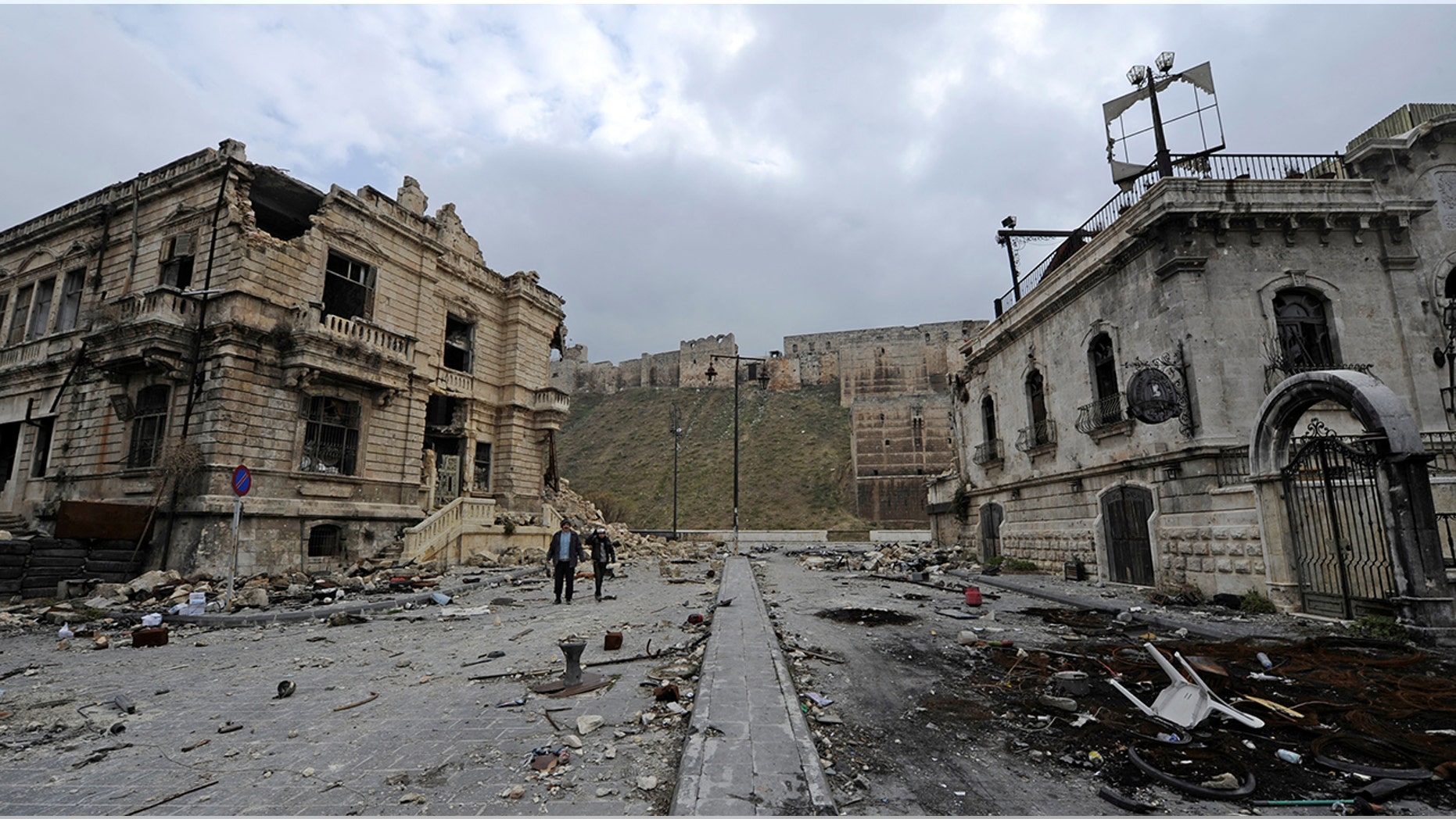 People walk past the old customs buildings (L) and Peoria restaurant (R) near Aleppo's historic citadel, in the government controlled area of the city, Syria December 17, 2016. REUTERS/Omar Sanadiki - RC1A5D700FD0