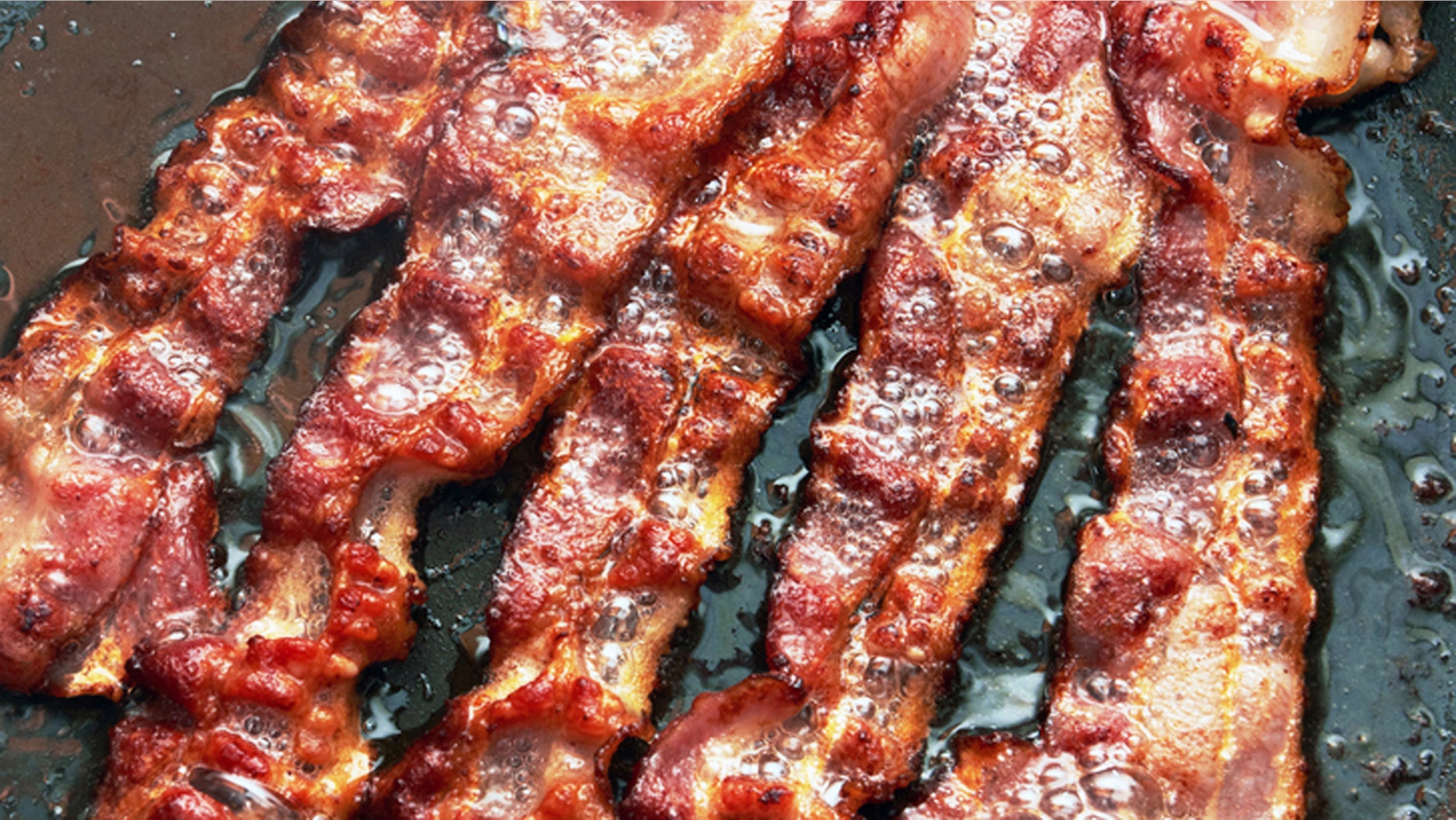Bacon slice being cooked in frying pan. Close up.