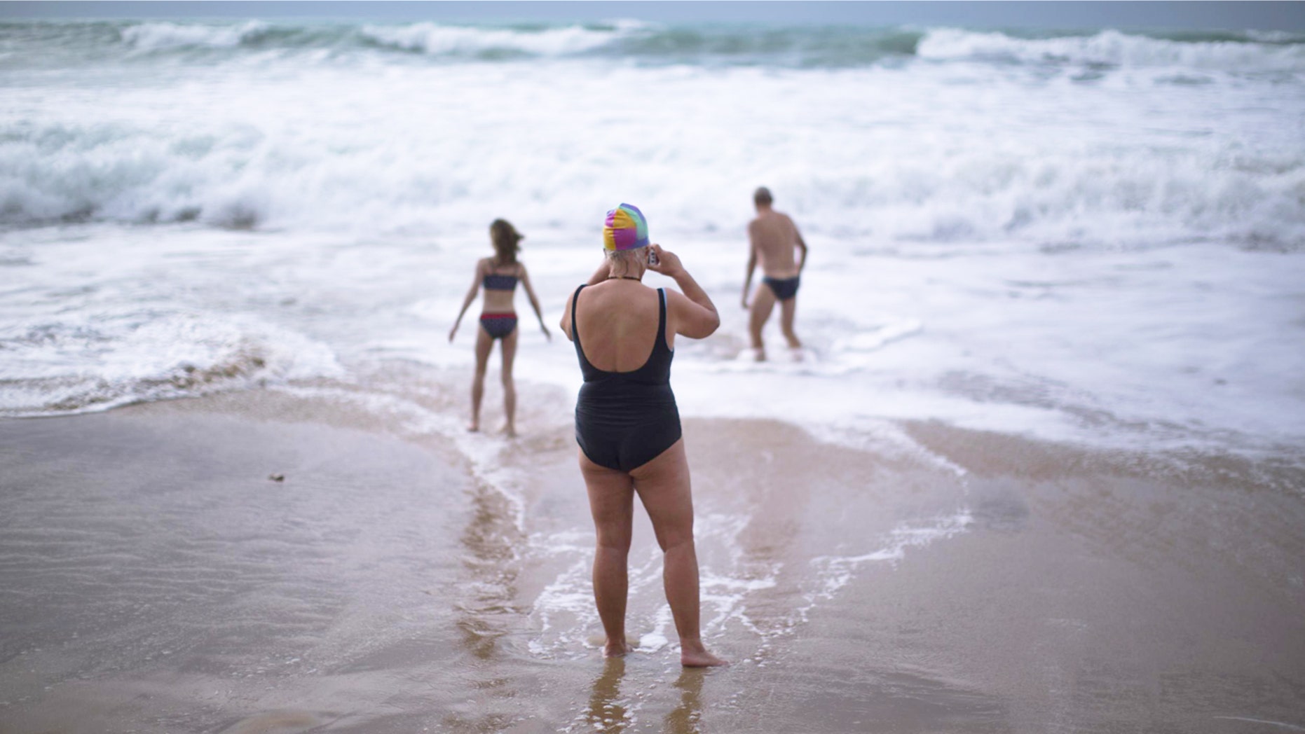 German tourists walk on the seashore as one of them takes a photograph, after swimming in the Atlantic ocean in a beach in Cadiz, southwest Spain.