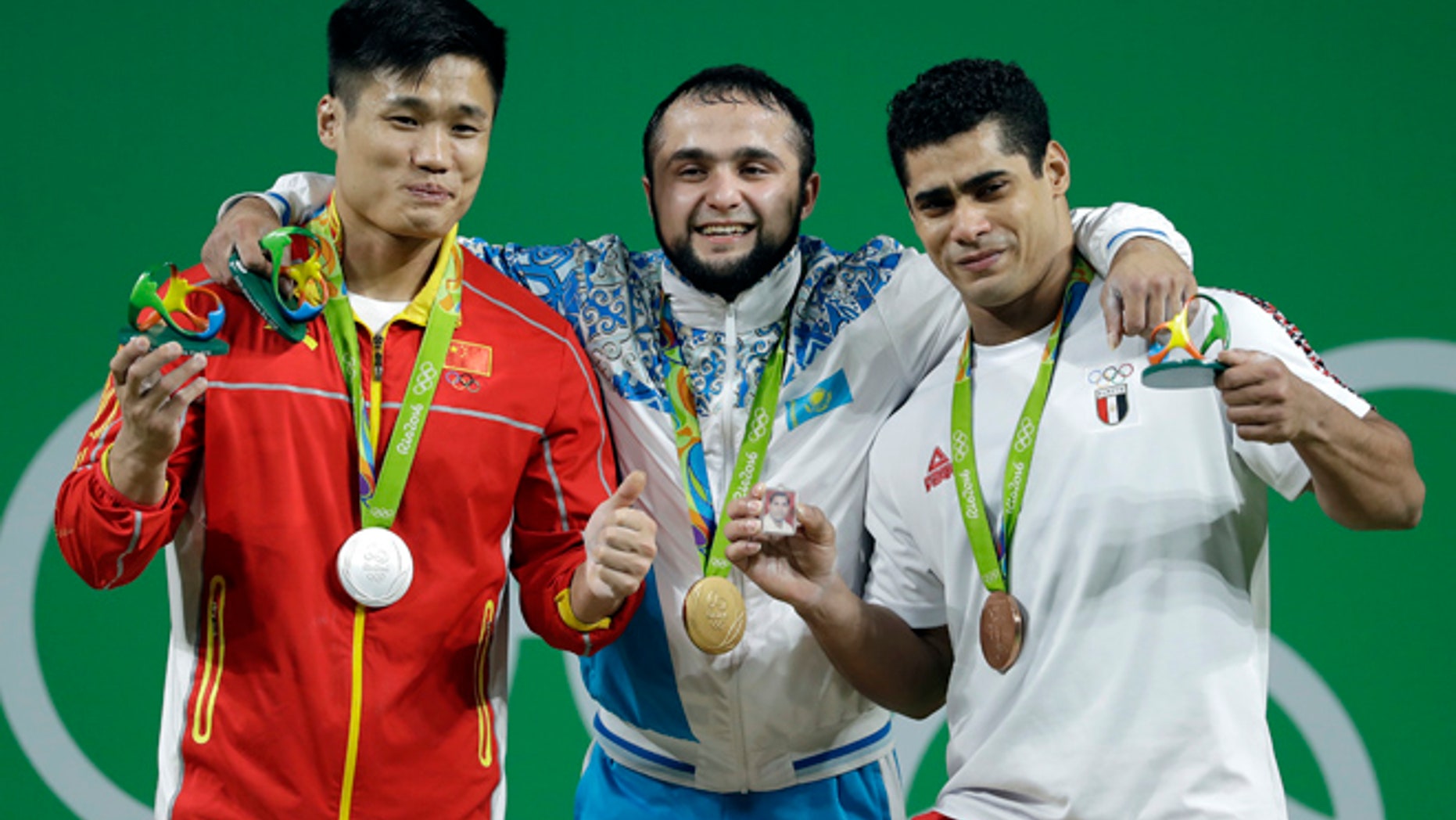 Gold medalist Nijat Rahimov, of Kazakhstan, center, stands with silver medalist Lyu Xiaojun, of China, left, and bronze medalist Mohamed Mahmoud, of Egypt, right, after the men's 77kg weightlifting competition at the 2016 Summer Olympics in Rio de Janeiro, Brazil, Wednesday, Aug. 10, 2016.