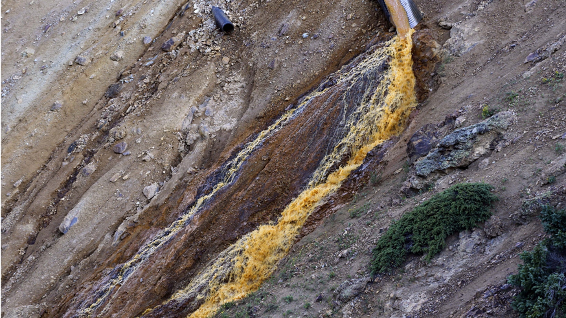 FILE--In this Aug. 13, 2015, file photo, wastewater flows from a trough and down a steep ravine at the site of the blowout at the Gold King mine which triggered a major spill of toxic wastewater, outside Silverton, Colo.Crumbling mine tunnels awash with polluted waters perforate the Colorado mountains, and scientists may one day send robots creeping through the pitch-black passages to study the mysterious currents that sometimes burst to the surface with devastating effects. (AP Photo/Brennan Linsley)
