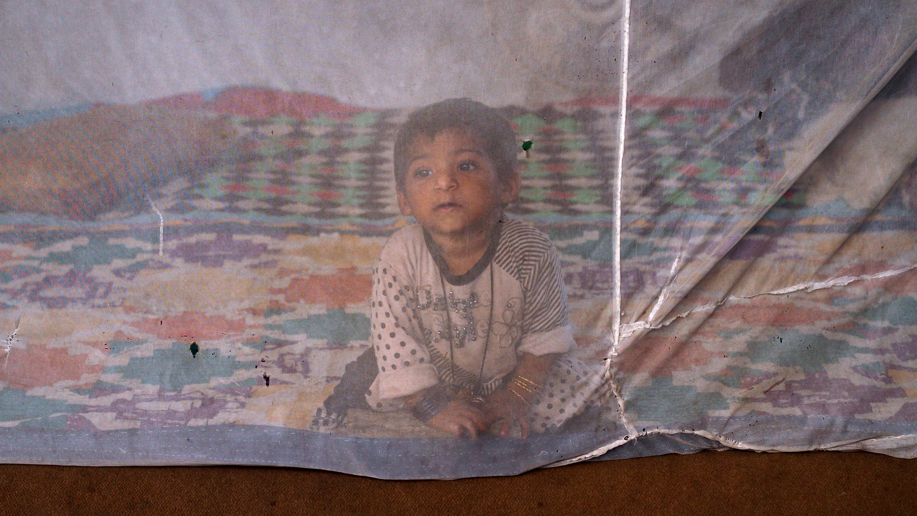 One and a half-year-old Reema sits under a mosquito net while taking shelter with her family under a bridge in Karachi October 19, 2011. REUTERS/Athar Hussain (PAKISTAN - Tags: SOCIETY) - RTR2SUMA