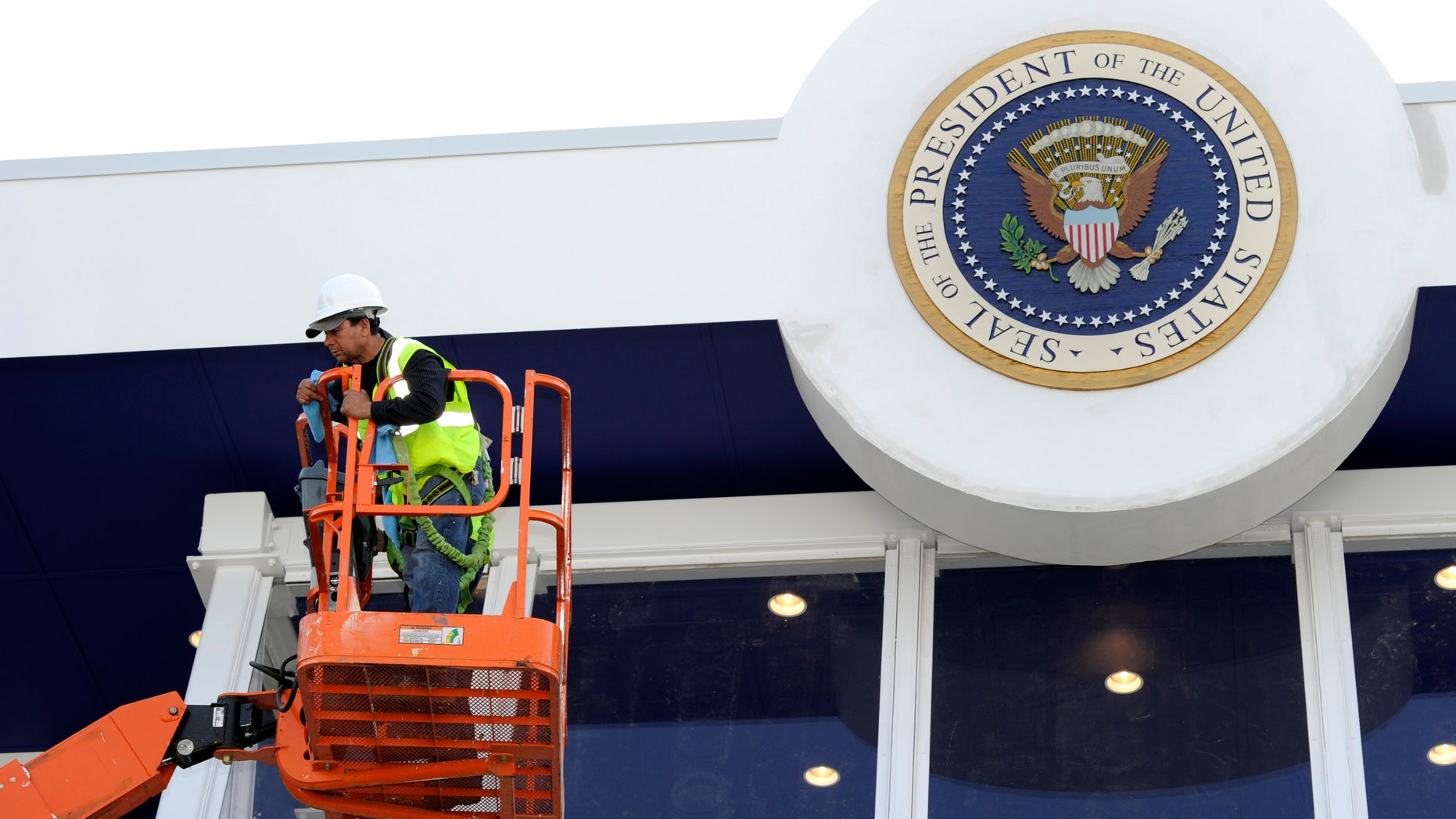 Workers use a hydraulic lift to position themselves to clean the bullet-proof glass under the Seal of the President on the inaugural reviewing stand in front of the White House in Washington January 12, 2013. U.S. President Barack Obama, family and dignitaries will watch the parade from the stand, after the Presidential Inauguration on January 21, 2013. REUTERS/Mike Theiler (UNITED STATES - Tags: POLITICS) - RTR3CD6F