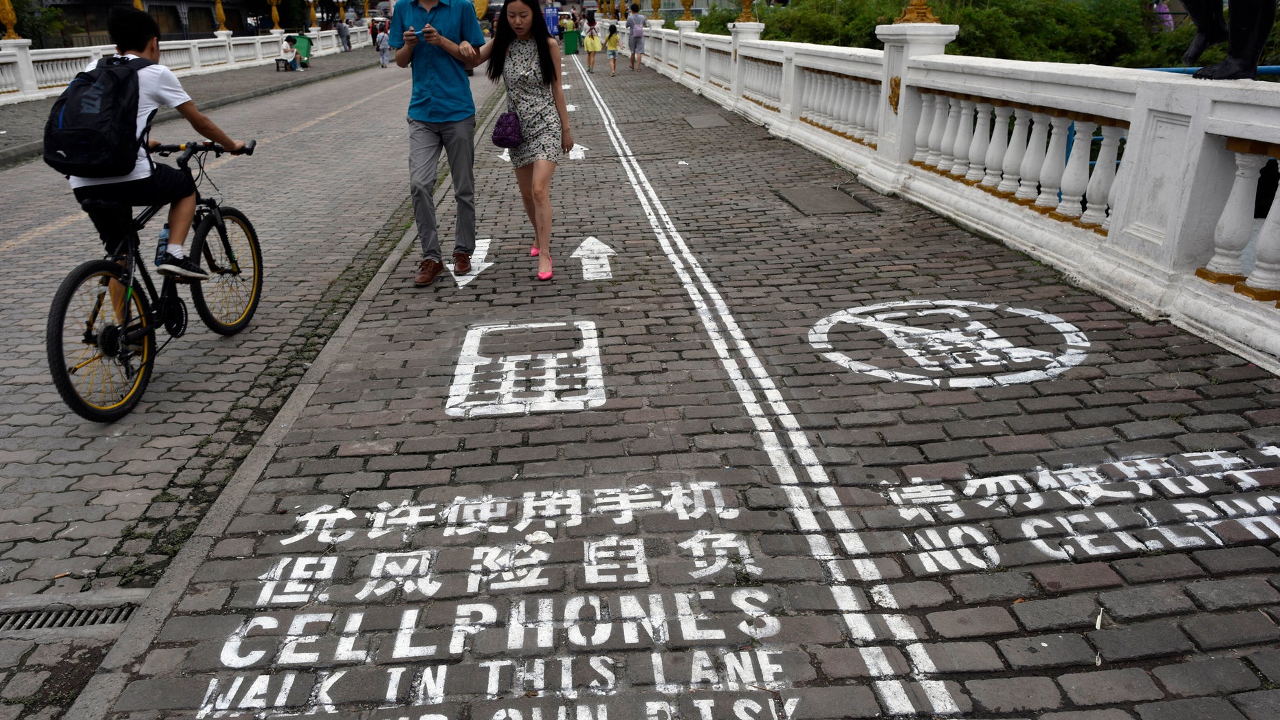 A man rides his bicycle as people walk on the "first mobile phone sidewalk in China", which was recently installed at a tourism area in Chongqing municipality, September 13, 2014. The mobile phone sidewalk in Chongqing was divided into two sides -- one was written with "Cellphones walk in this lane at your own risk" while the other with "No cellphones", as an attempt to reduce pedestrian incidents, local media reported. Picture taken September 13, 2014. REUTERS/China Daily