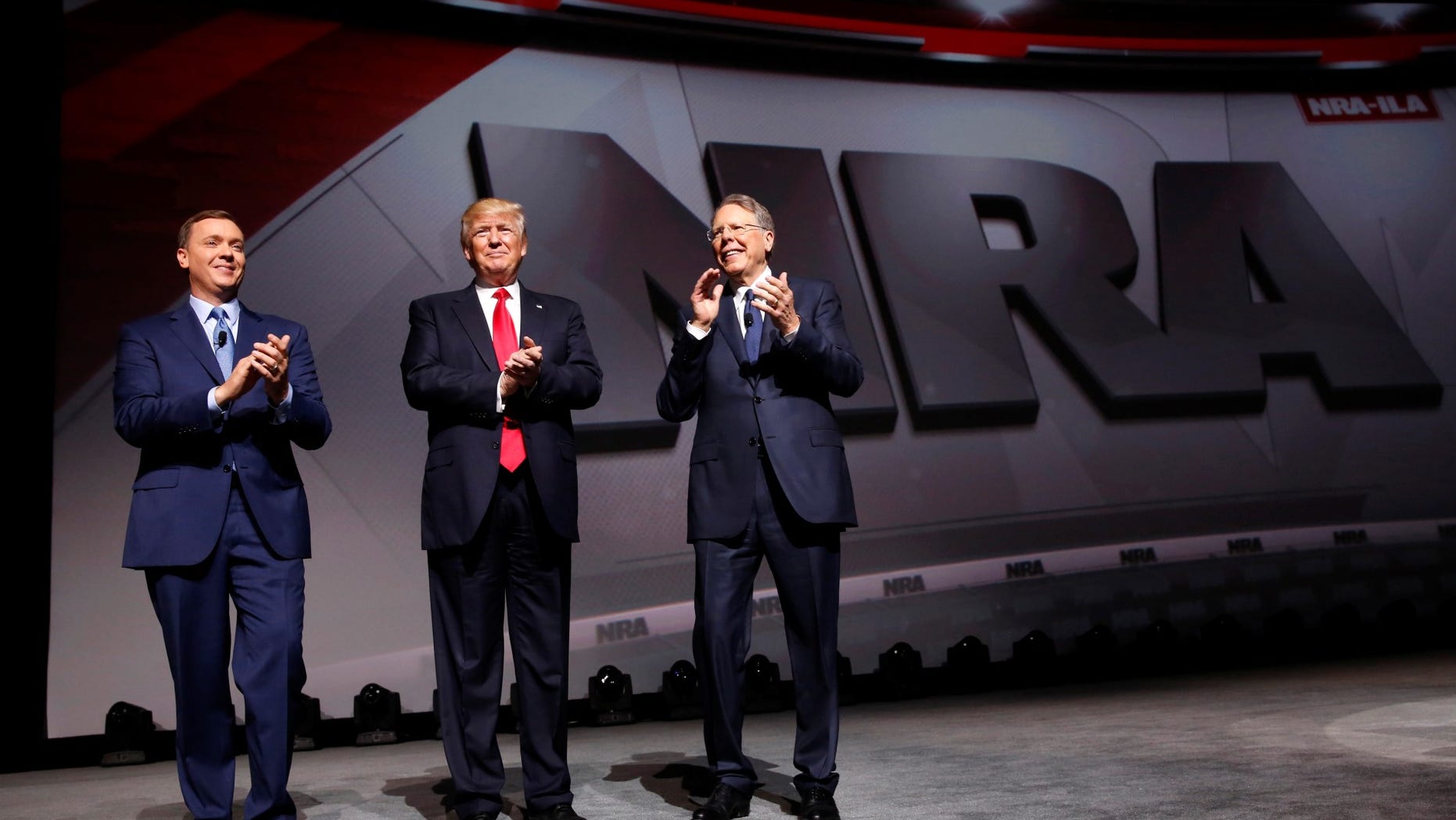 FILE -- April 28, 2017: NRA Executive Director Chris Cox (L) and Executive Vice President and CEO Wayne LaPierre (R) welcome President Donald Trump (C) onstage to deliver remarks at the National Rifle Association (NRA) Leadership Forum at the Georgia World Congress Center in Atlanta, Georgia.