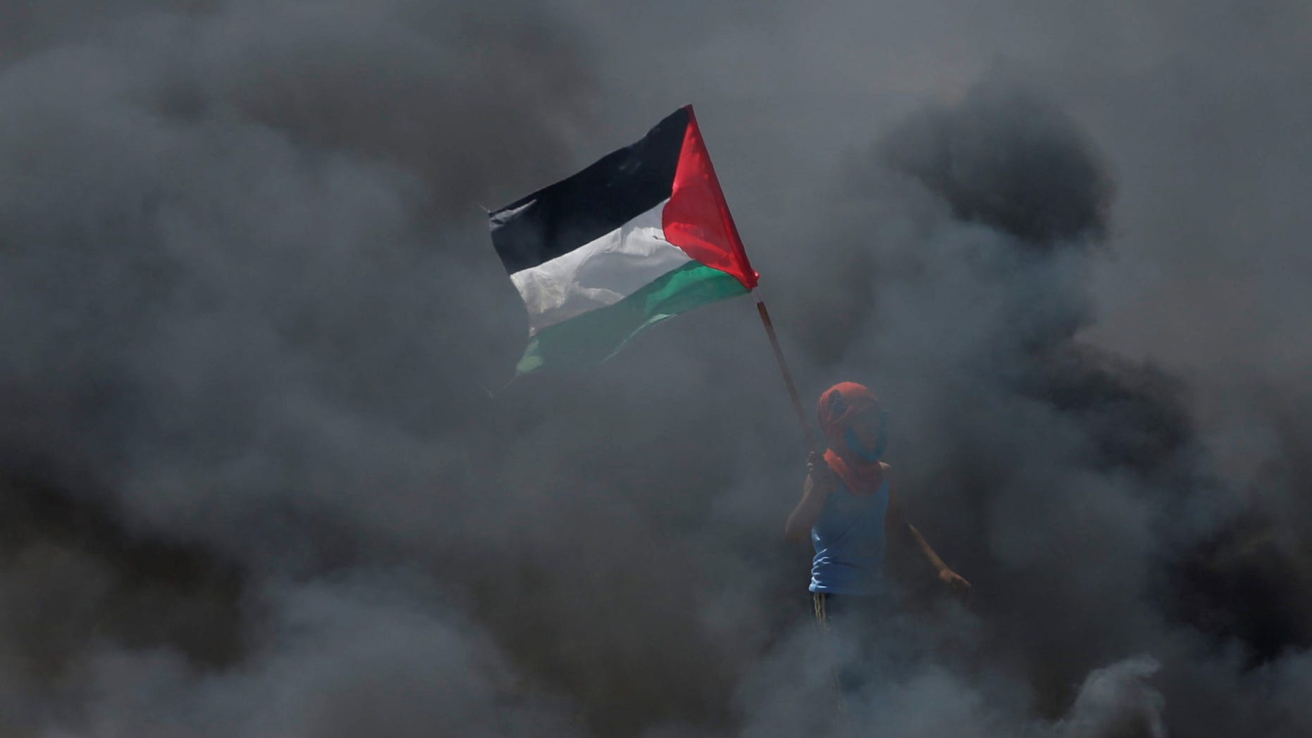 FILE -- A boy holds a Palestinian flag as he stands amidst smoke during a protest against U.S. embassy move to Jerusalem.
