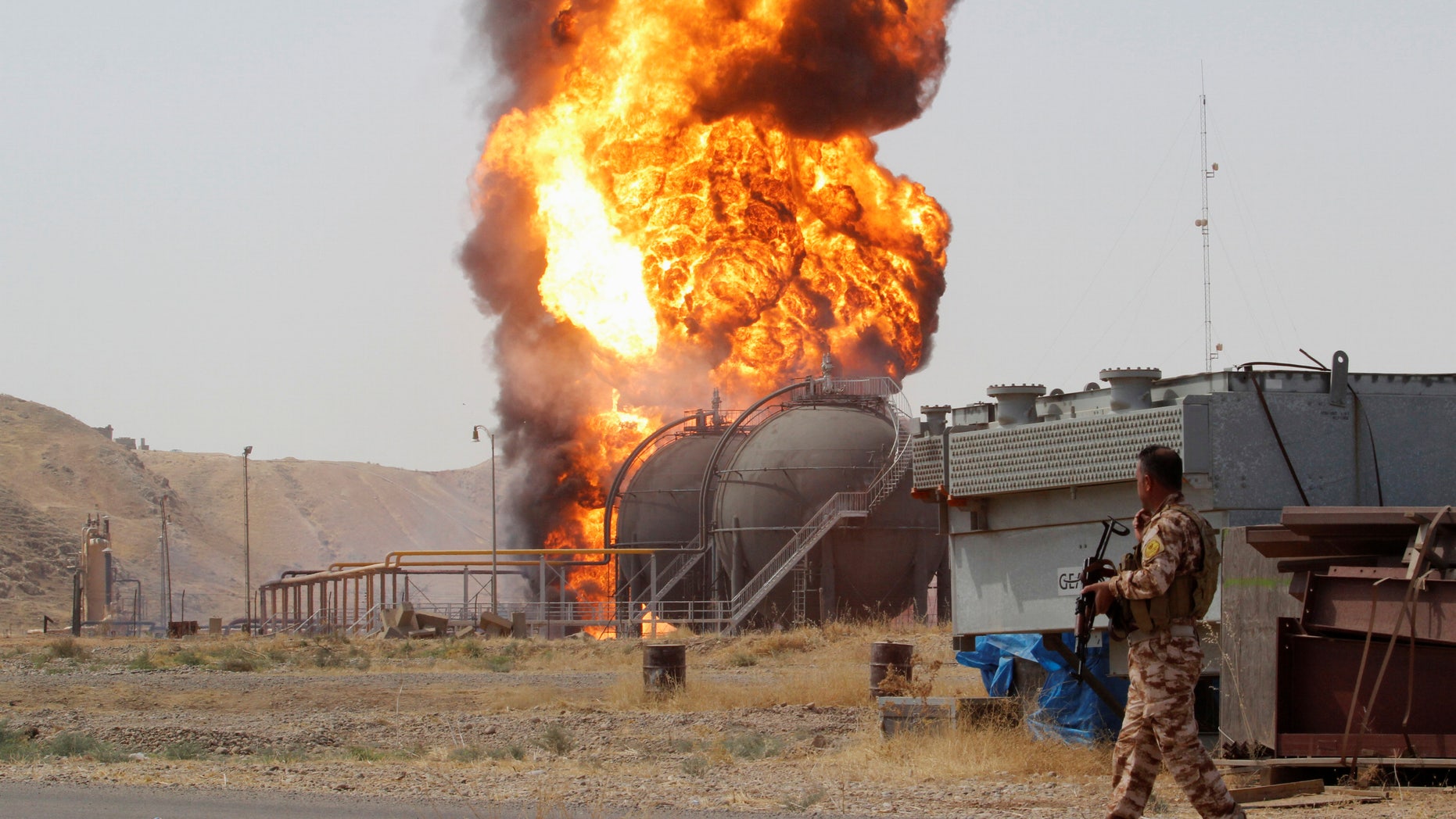 A member of the Kurdish Peshmerga forces walks as smoke rises after an attack at Bai Hassan oil station, northwest of Kirkuk, Iraq, July 31, 2016. REUTERS/Ako Rasheed - RTSKFNM