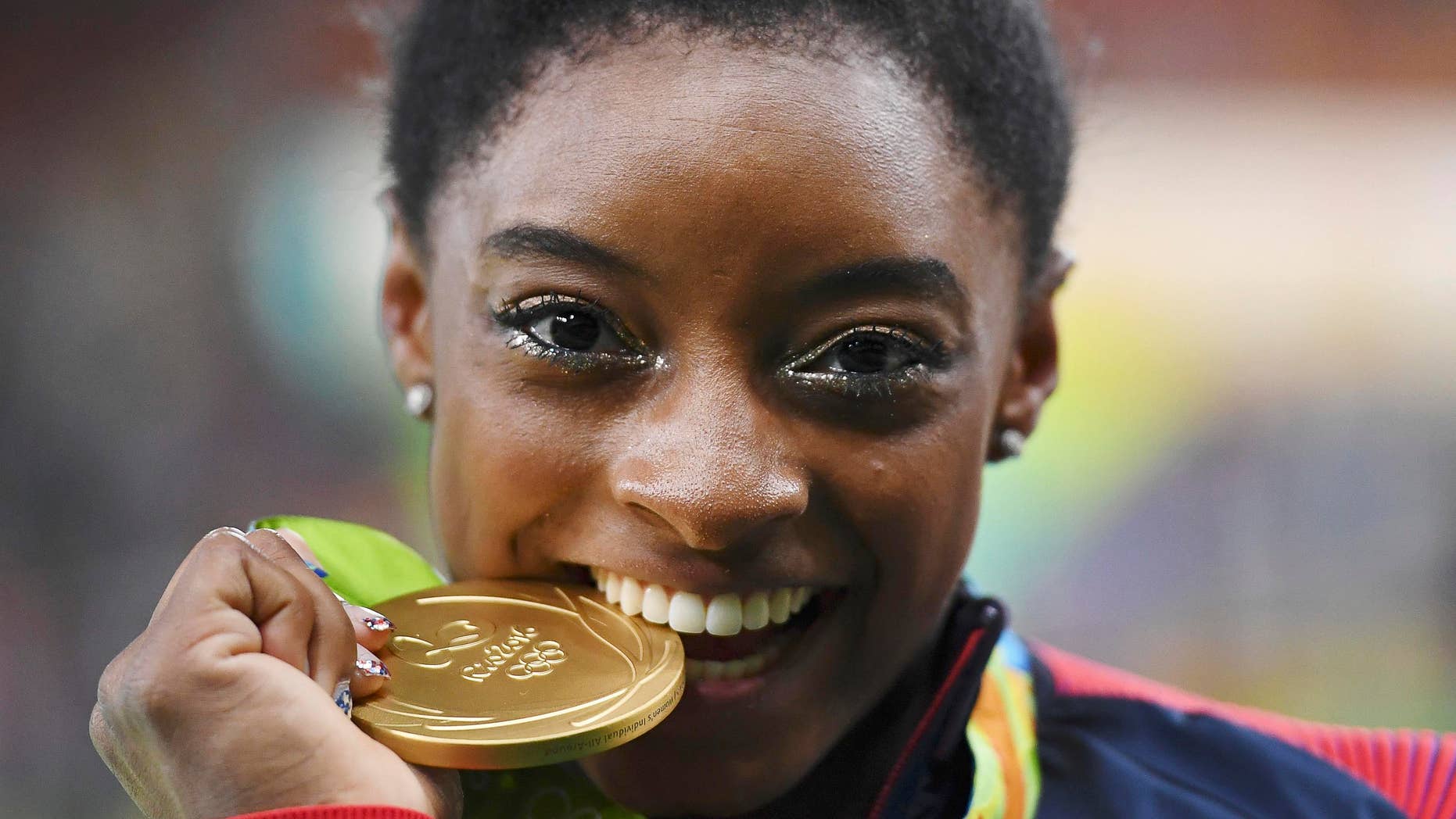 2016 Rio Olympics - Artistic Gymnastics - Victory Ceremony - Women's Individual All-Around Victory Ceremony - Rio Olympic Arena - Rio de Janeiro, Brazil - 11/08/2016. Simone Biles (USA) of USA bites her gold medal on the podium after winning the women's individual all-around final. REUTERS/Dylan Martinez TPX IMAGES OF THE DAY. FOR EDITORIAL USE ONLY. NOT FOR SALE FOR MARKETING OR ADVERTISING CAMPAIGNS. - RTSMS3U