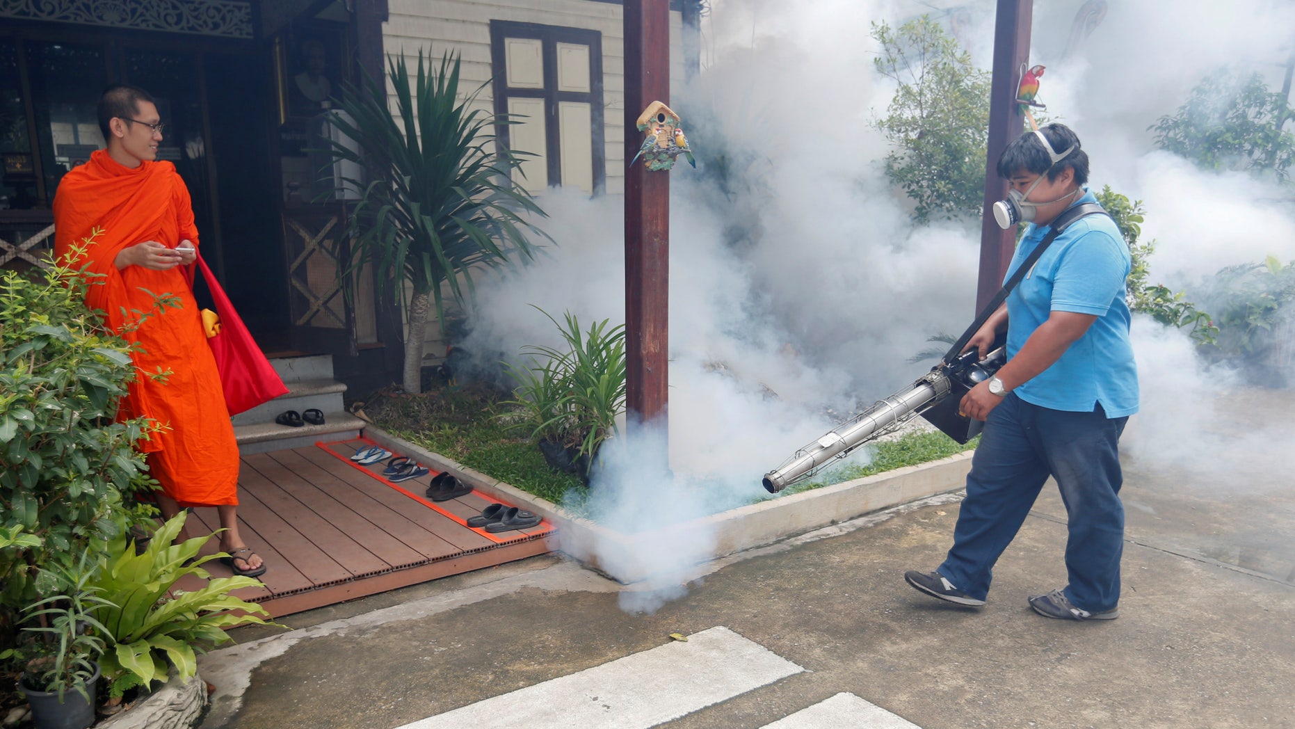 A city worker fumigates the area to control the spread of mosquitoes as a Buddhist monk looks on at a temple in Bangkok, Thailand, September 14, 2016.