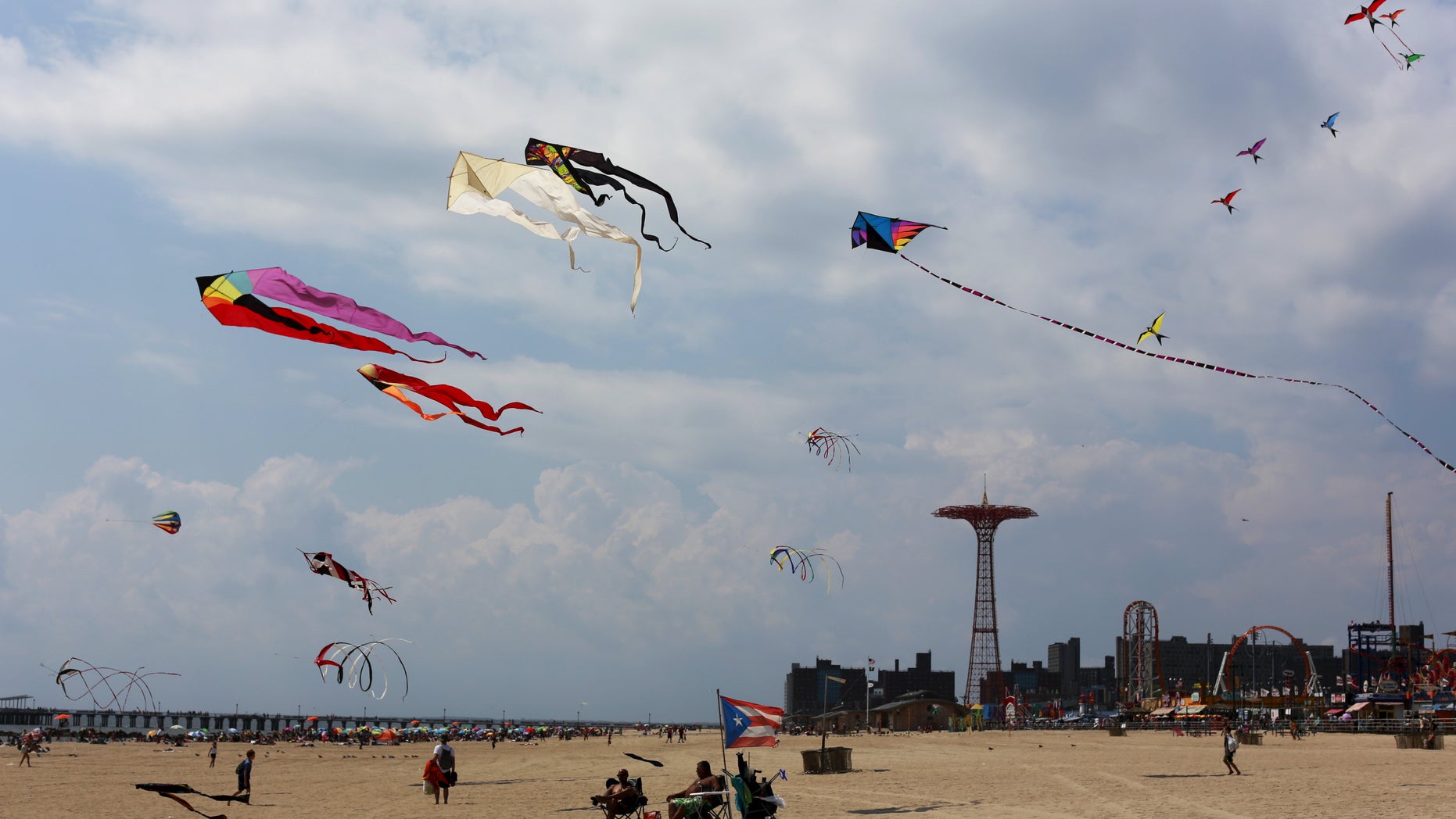 Kites fly in the sky as people sit and walk on the beach at Coney Island in the Brooklyn borough of New York, August 19, 2015. REUTERS/Shannon Stapleton - RTX1OUN4