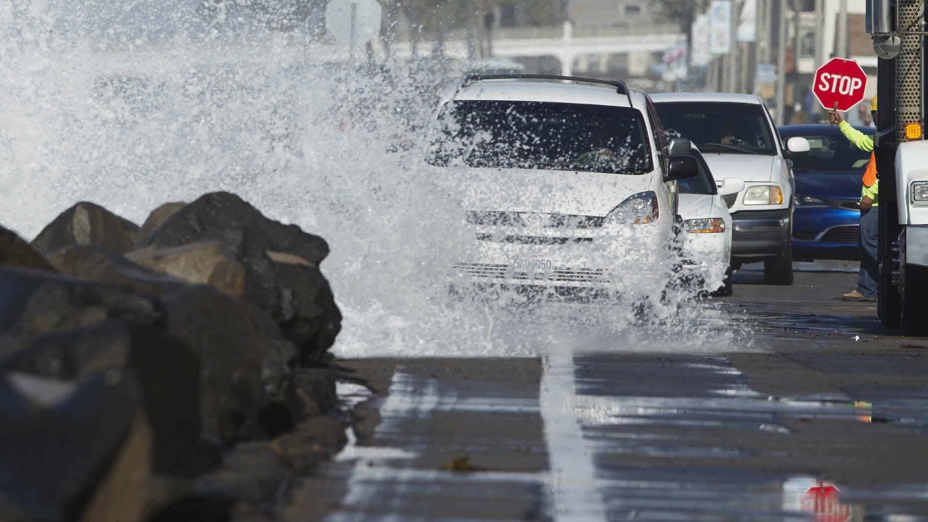 Drivers make their way along a beach road as a wave crashes onto the street due to a combination of high tides and high surf in Oceanside, California October 27, 2015.