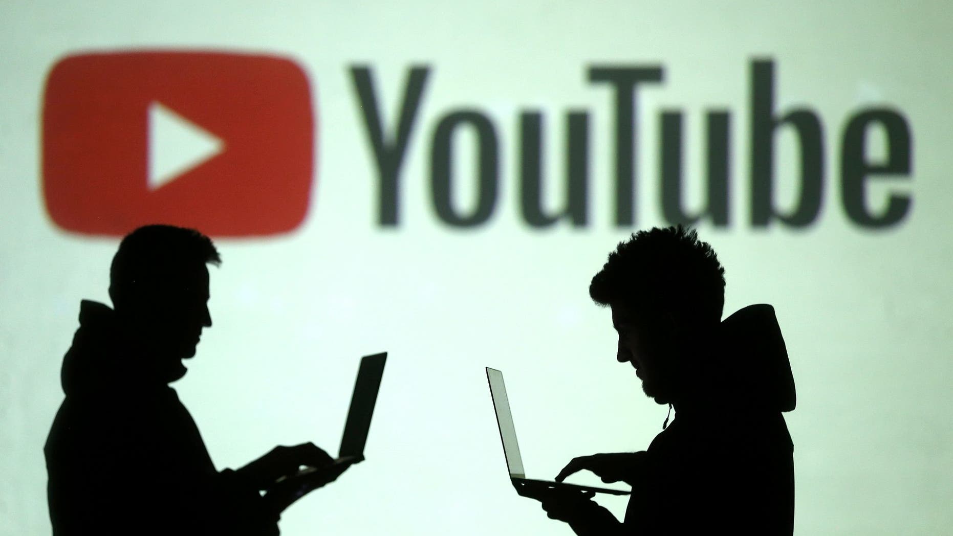 Silhouettes of mobile device users are seen next to a screen projection of Youtube logo in this picture illustration taken March 28, 2018. REUTERS/Dado Ruvic/Illustration - RC1502FFC0B0