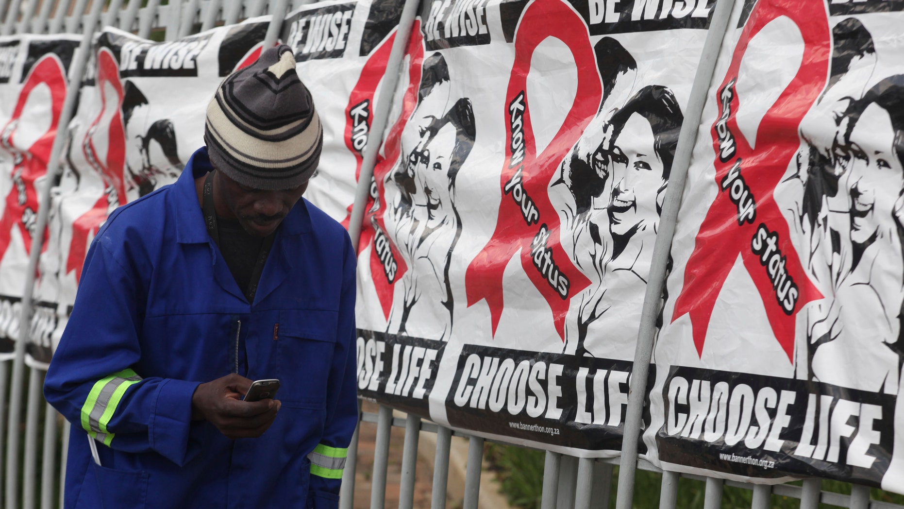 Dec. 1, 2014: In this file photo, a man makes a call on a mobile phone as he passes World AIDS Day banners on the perimeter of an office building in Sandton, Johannesburg, South Africa.