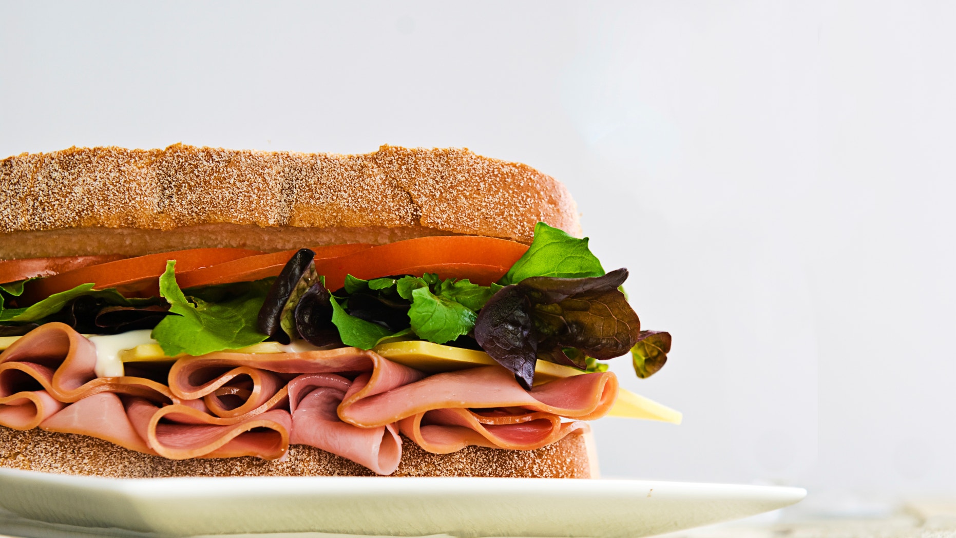A gourmet sandwich of ham, cheese, lettuce, tomato and mayonaise isolated on white.