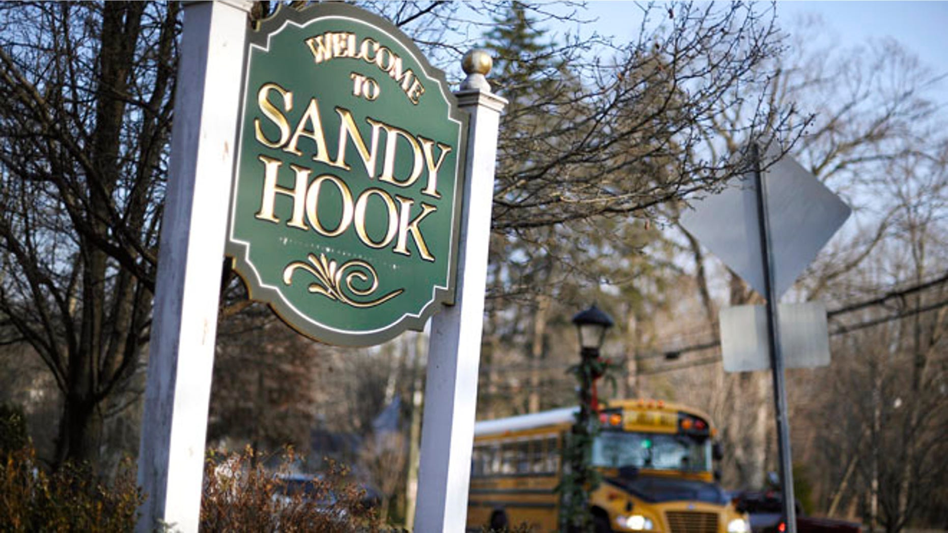 A school bus drives past a lamppost decorated for the holidays, and a sign reading Welcome to Sandy Hook, in Newtown, Conn.