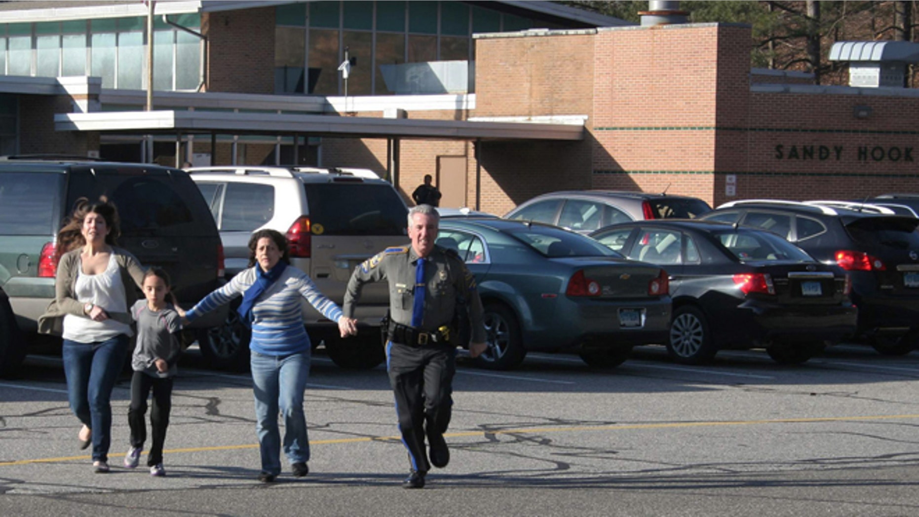 Dec. 14, 2012: In this file photo provided by the Newtown Bee, a police officer leads two women and a child from Sandy Hook Elementary School.