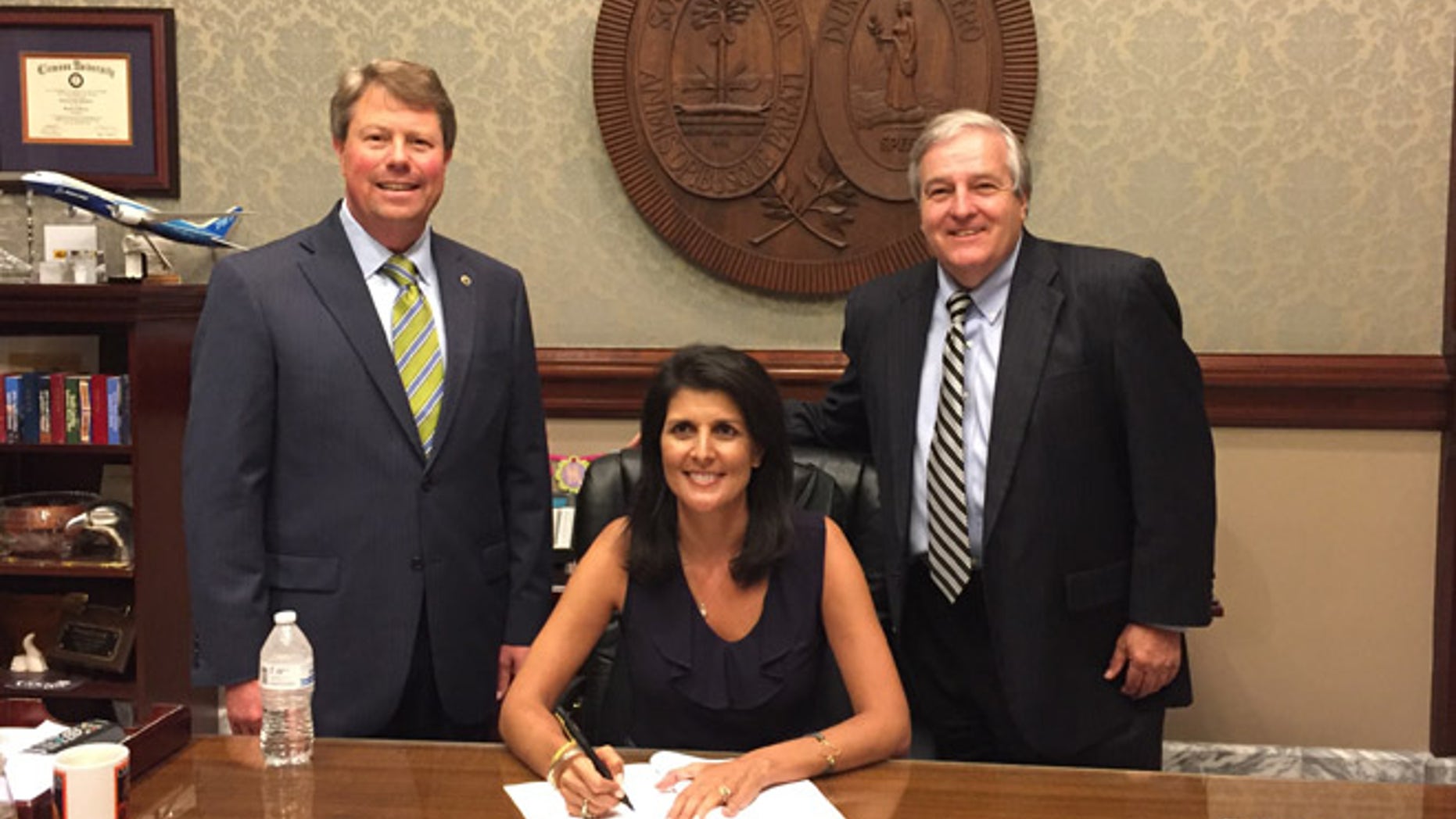 Haley (seated) signed the bill as Huggins, (l.), and former state Sen. Don Vaughan, (r.), looked on.