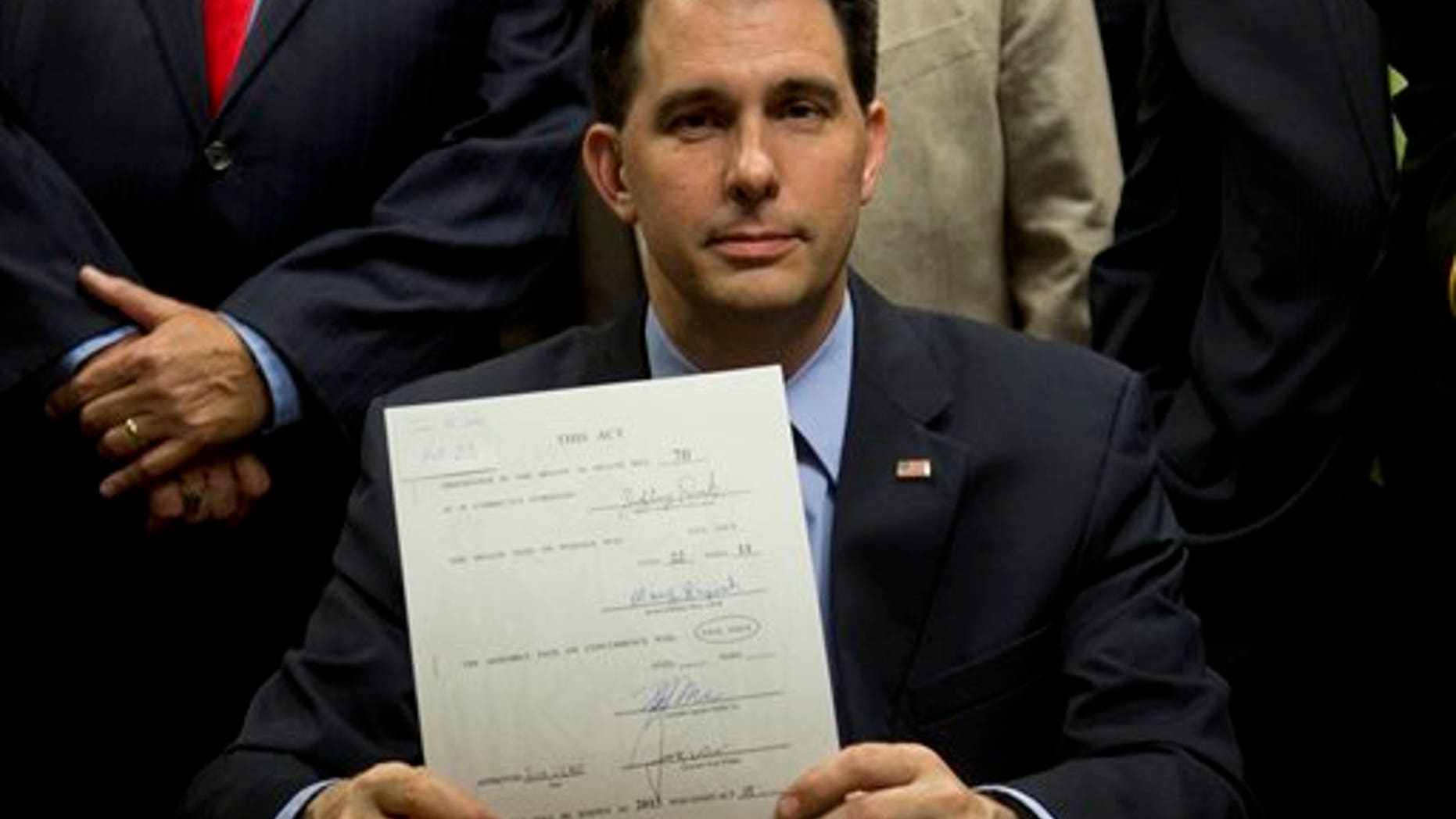 FILE -- June. 24, 2015: Wisconsin Gov. Scott Walker holds up a bill after signing it at the Milwaukee County Sheriff's office that eliminates a 48-hour waiting period for handgun purchases. (AP Photo/Jeffrey Phelps)