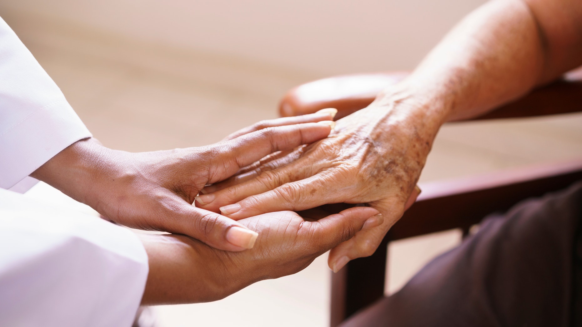 Old people in geriatric hospice: Aged patient receives the visit of a female black doctor. They shake their hands and talk in the hospital.