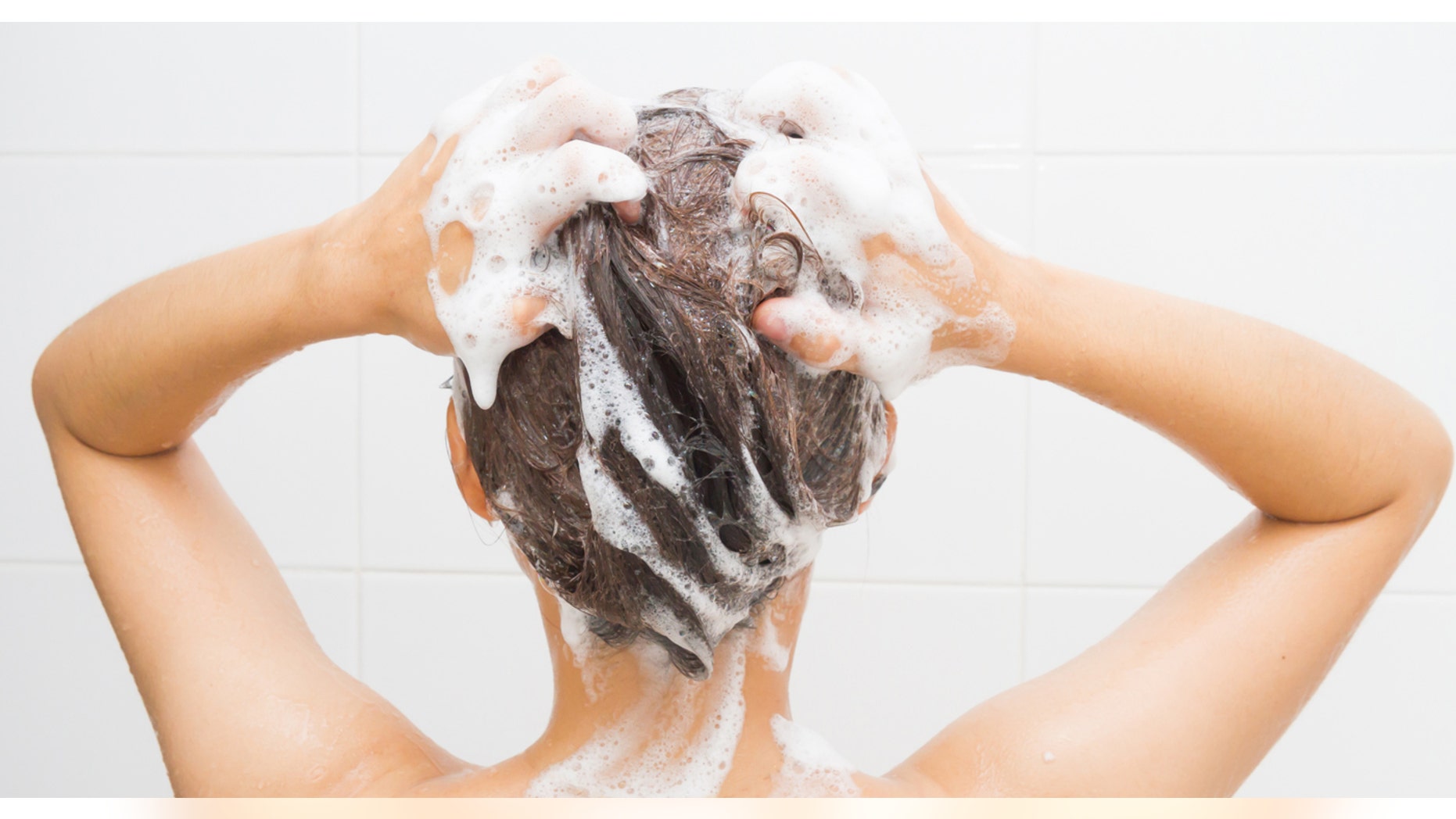 Woman washing her hair on white tiles background.