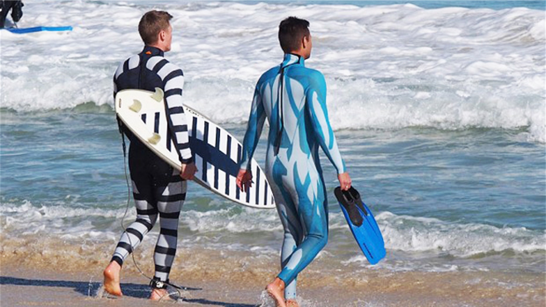 July 18, 2013: A surfer and a diver wearing wetsuits displaying the two styles of shark deterrent technology, with the surfer holding a surfboard also showing the new design.