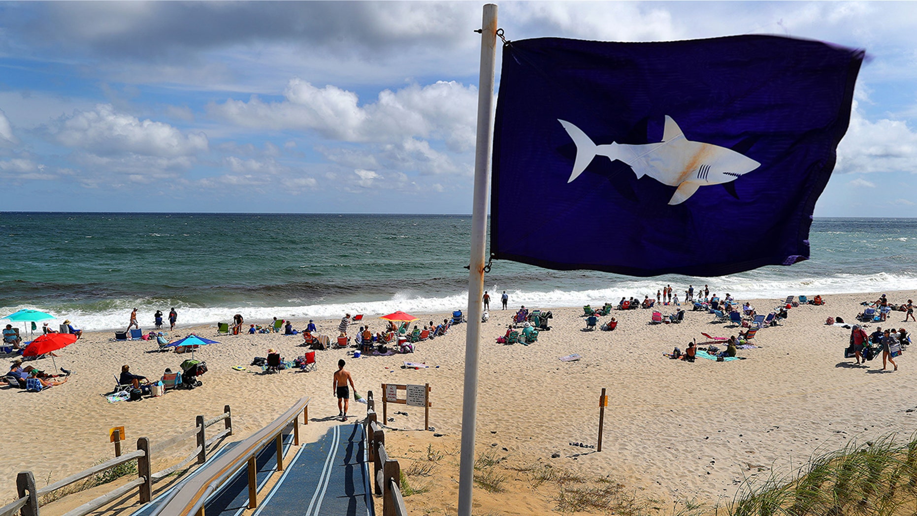 A flag warning Cape Cod visitors of sharks blows in the wind at an entrance point to Nauset Beach in Orleans, Mass., on Aug. 31, 2018.