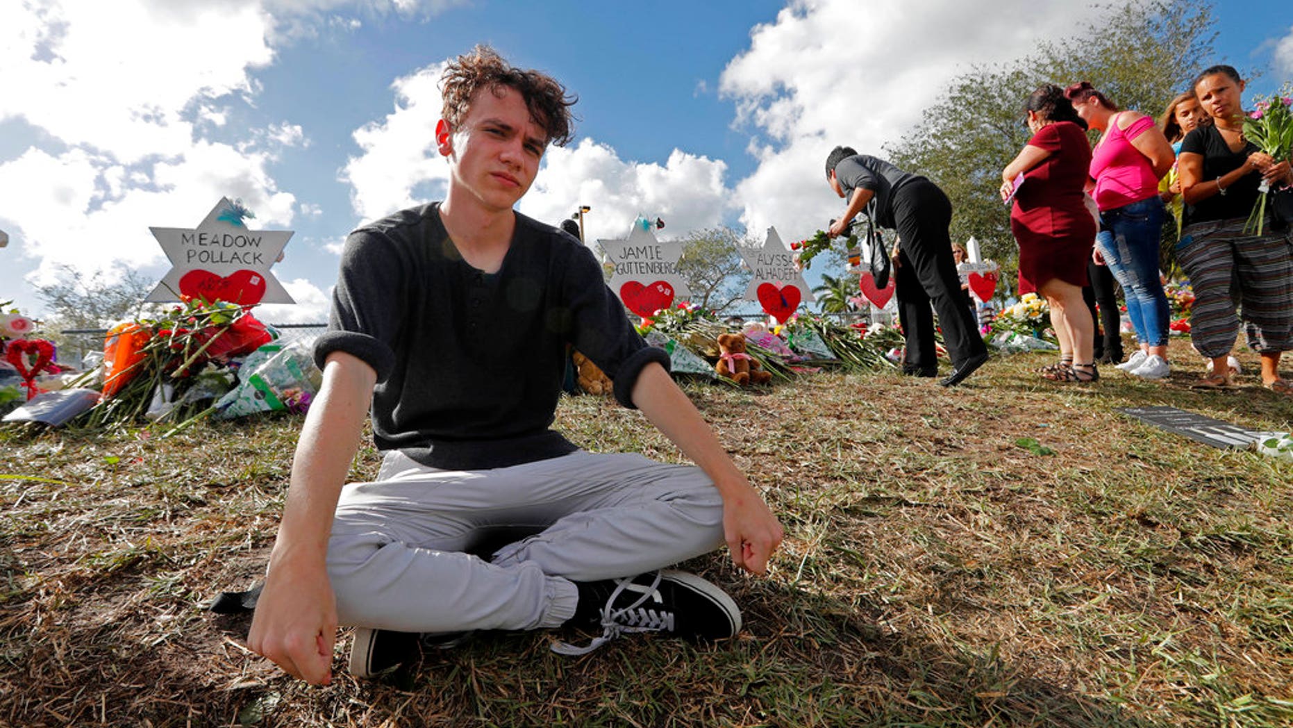 FILE- In this Feb. 19, 2018, file photo, Chris Grady, a student at Marjory Stoneman Douglas High School, sits at a memorial in Parkland, Fla., for those slain in the Feb. 14 school shooting. Grady who had planned to join the U.S. Army before the shooting, has withdrawn his enlistment and will now work for the March for Our Lives movement. (AP Photo/Gerald Herbert, File)