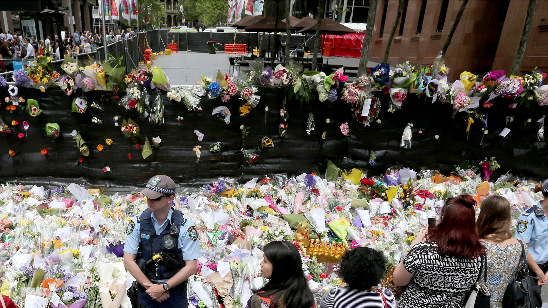 Dec. 17, 2014: Police stand watch over flower tributes to the shooting victims on the footpath outside the the cordoned off area outside the Lindt cafe in the central business district of Sydney.