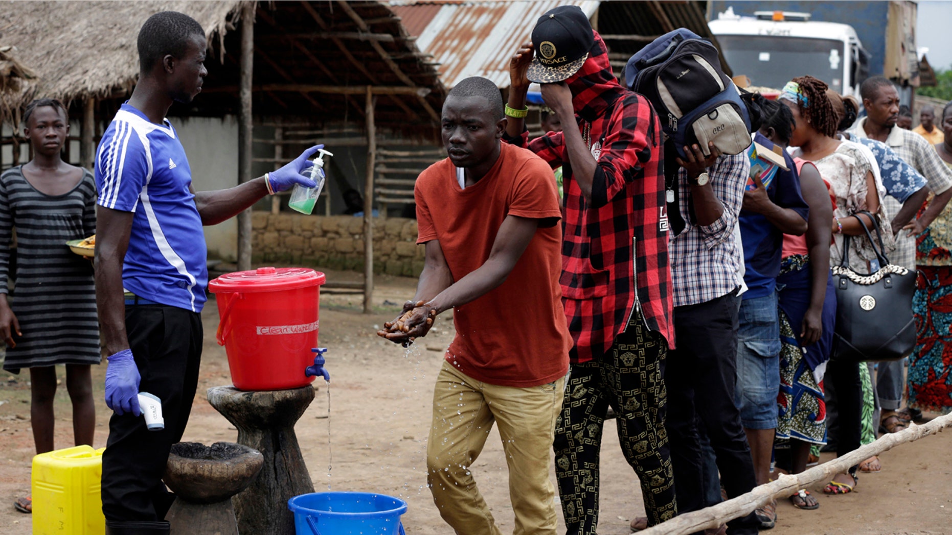 FILE-In this file photo taken Wednesday, Aug. 12, 2015, a man checks people's temperature and helps to wash their hands as they leave an Ebola quarantined area on the outskirts of Freetown, Sierra Leone. (AP Photo/Sunday Alamba, File)