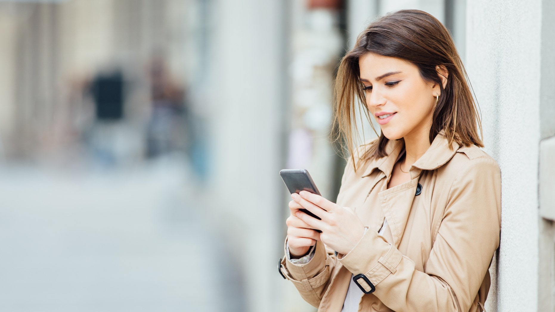 Beautiful young woman standing at the street and using her mobile phone