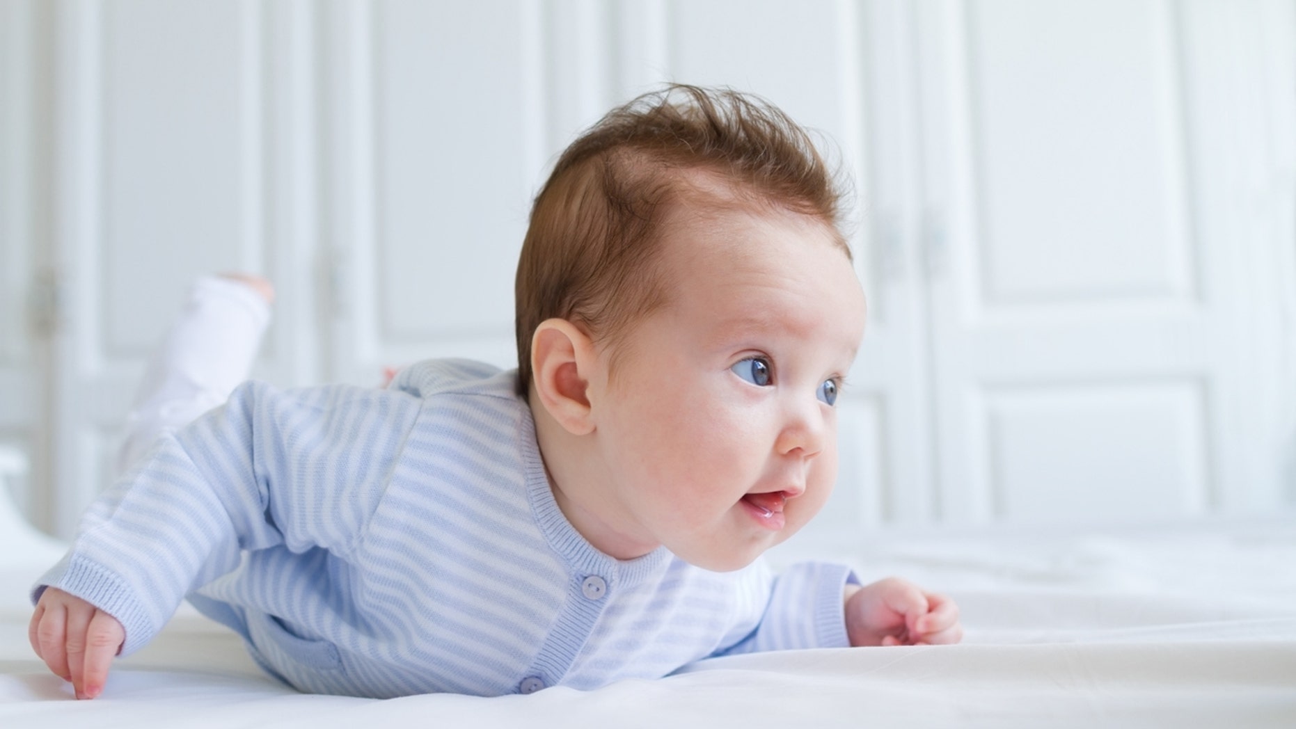 Smiling baby tummy time in a white nursery