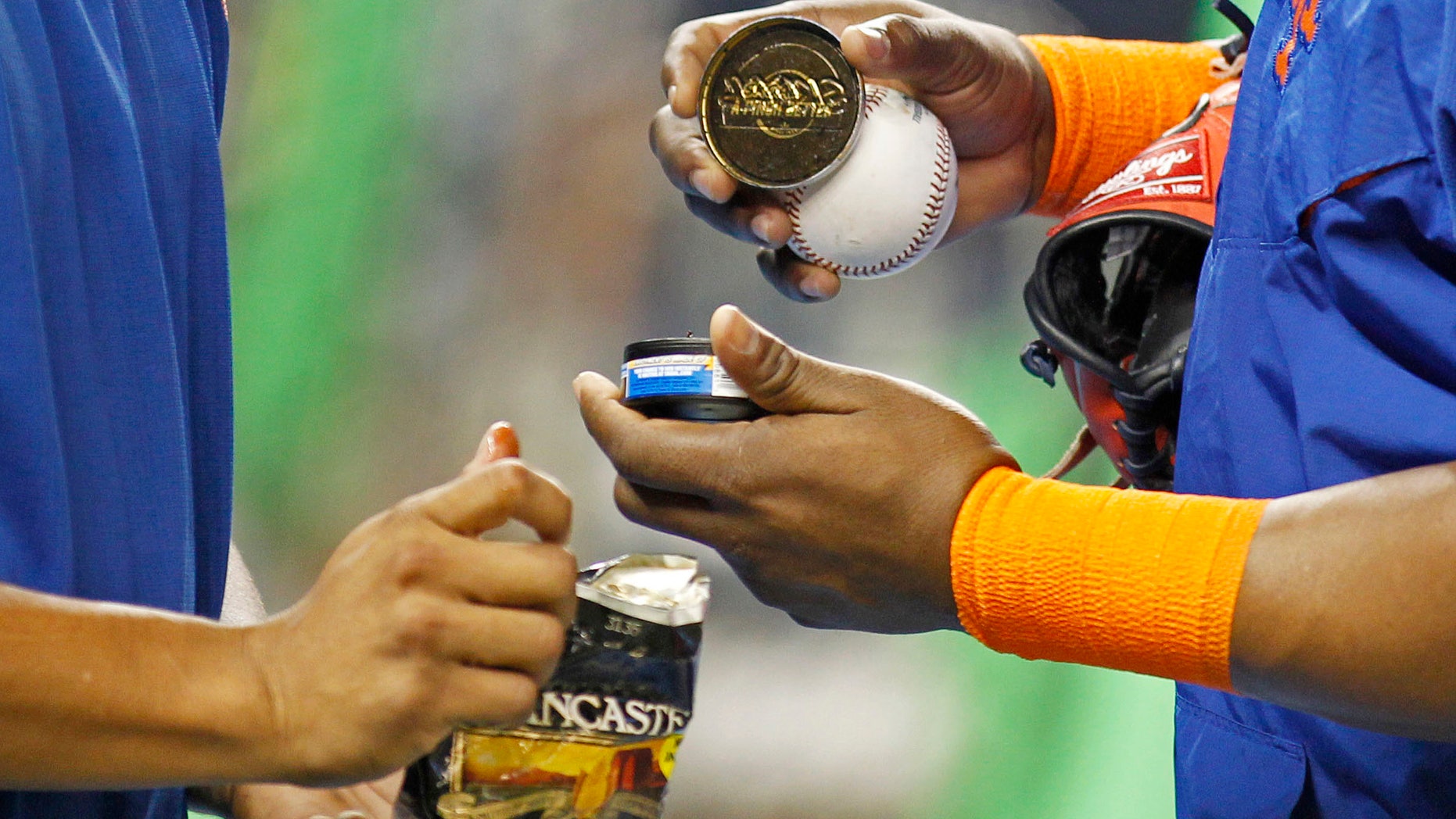 FILE - In this Sept. 5, 2015, file photo, New York Mets players hold tobacco products during batting practice before the team's baseball game against the Miami Marlins in Miami. A person familiar with the negotiations says Major League Baseball and its players' union agreed to ban smokeless tobacco for all new big leaguers. The person spoke on condition of anonymity Wednesday night, Nov. 30, 2016, because the ban is among the details of the sport's new collective bargaining agreement that have not been announced. The ban does not apply to any player who already has at least one day of major league service. (AP Photo/Joe Skipper, File)